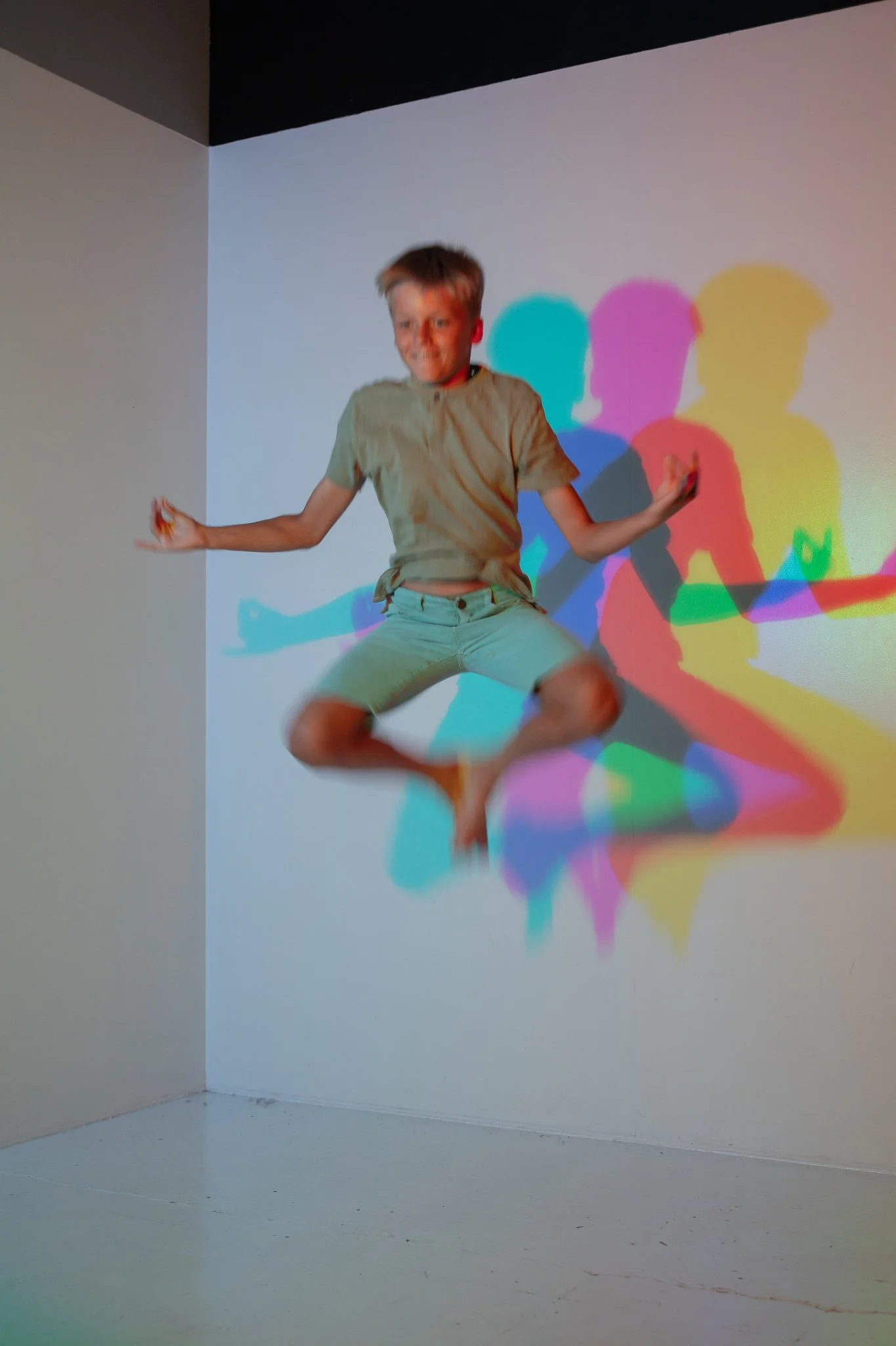 A person jumping with shadow cast on the wall behind them, showing multiple colored silhouettes.