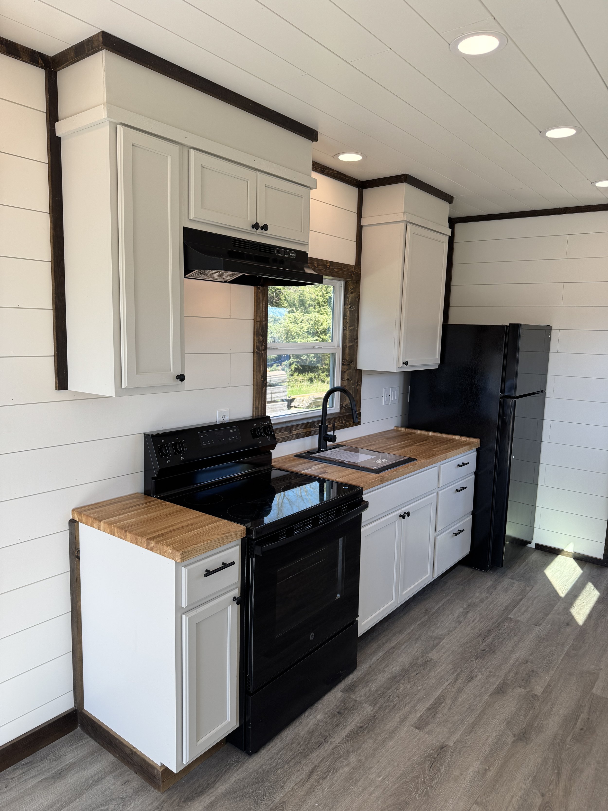 Modern kitchen inside our completed 40’ high-cube shipping container home in Paris, Texas, featuring white cabinets, black stove, wood countertops, and stainless steel sink – part of our $65,000 fully finished turnkey model