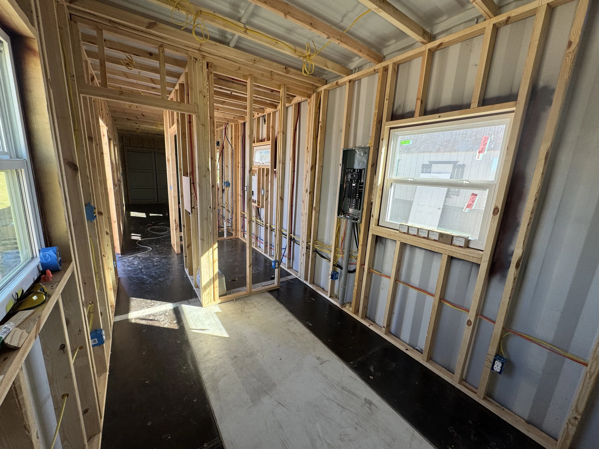 Interior framing, plumbing, and electrical in turnkey shipping container home construction in Paris Texas showing exposed wood framing, PEX plumbing lines, and electrical wiring before spray foam insulation
