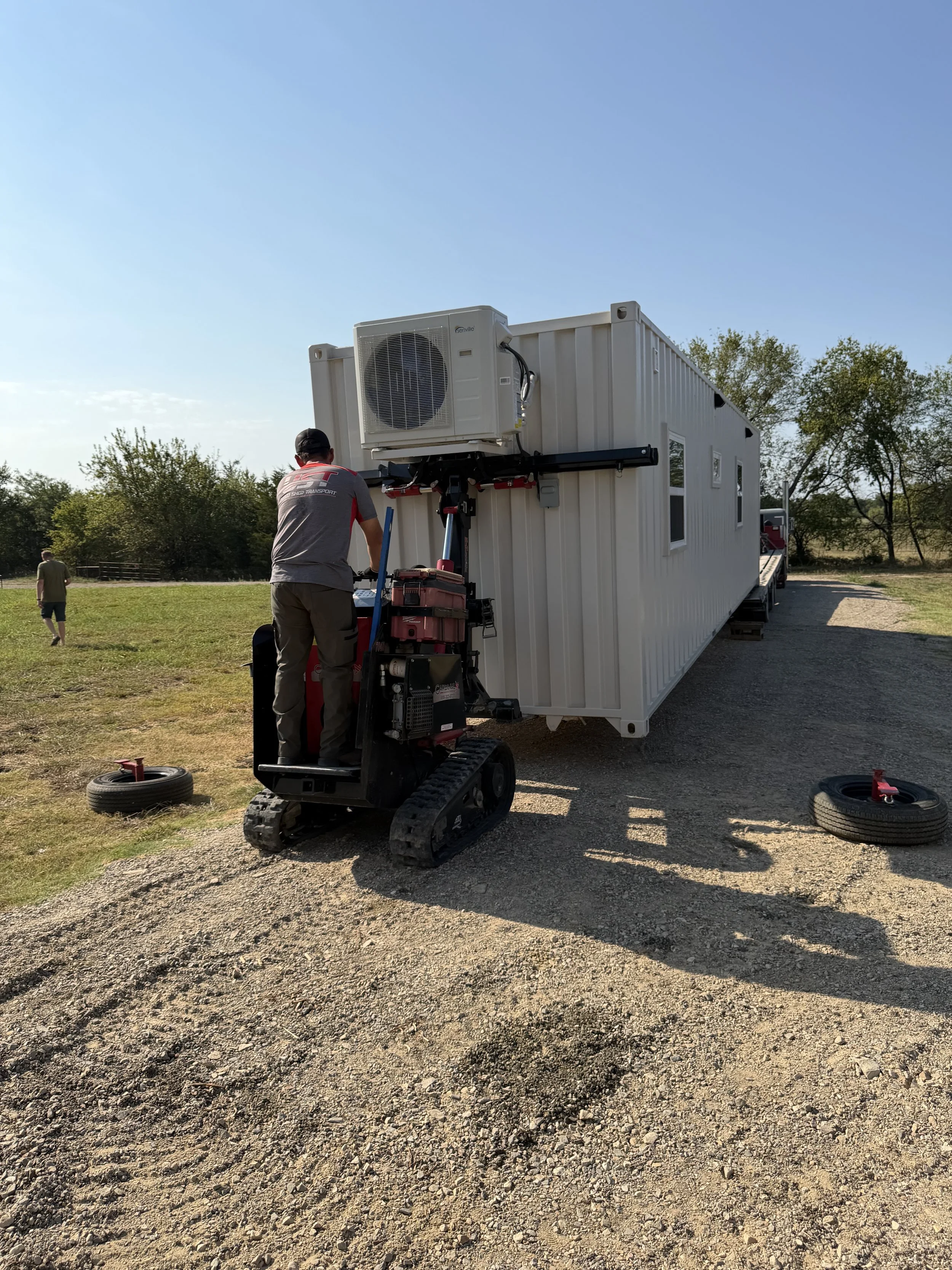 Shipping container home being loaded onto a tilt-deck trailer using a container mule for positioning and transport.