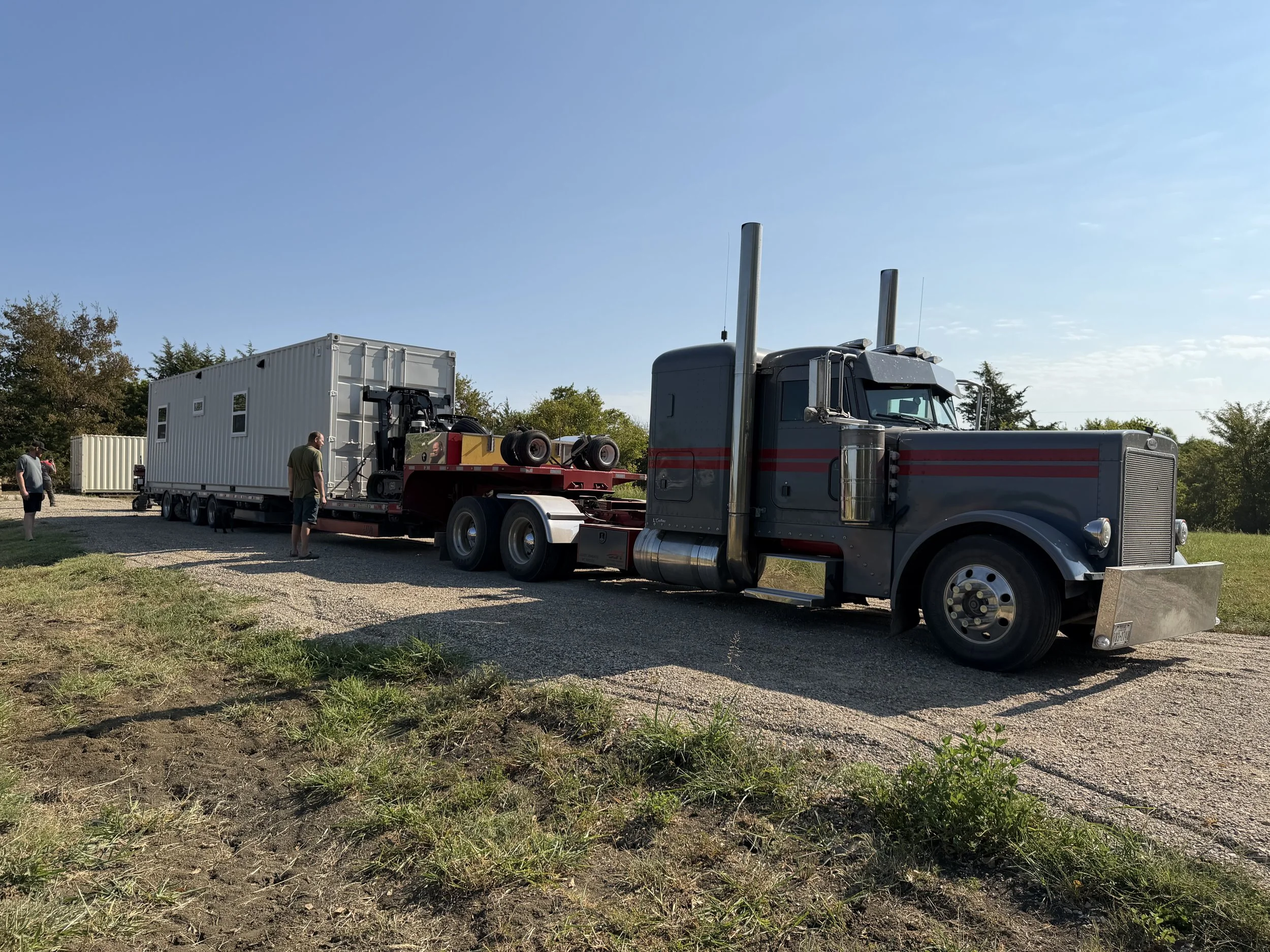 Shipping container home secured on a trailer behind a semi truck, ready for delivery to the customer.