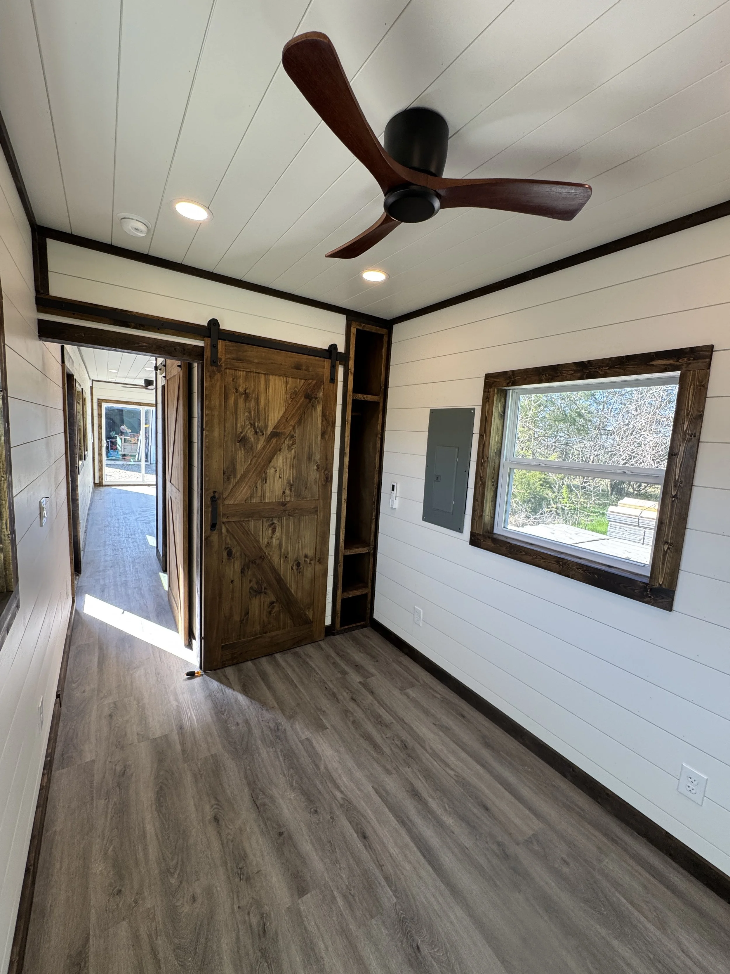 Interior hallway of our completed 40’ high-cube shipping container home in Paris, Texas, featuring a wooden sliding barn door and ceiling fan – part of our $65,000 fully finished turnkey model