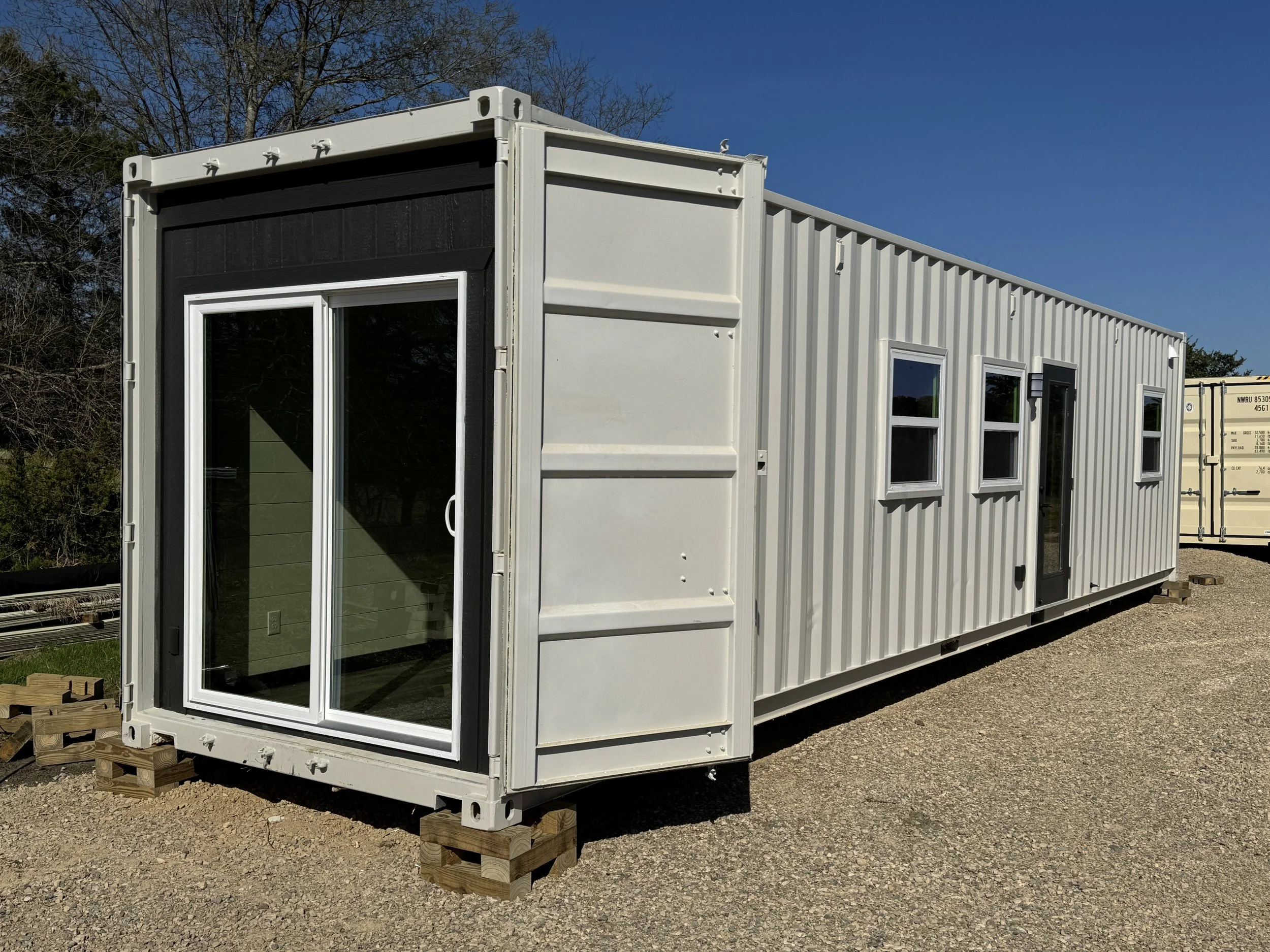 Turnkey shipping container home exterior in Paris Texas with large sliding glass patio doors, white steel siding, and gravel lot under clear blue sky