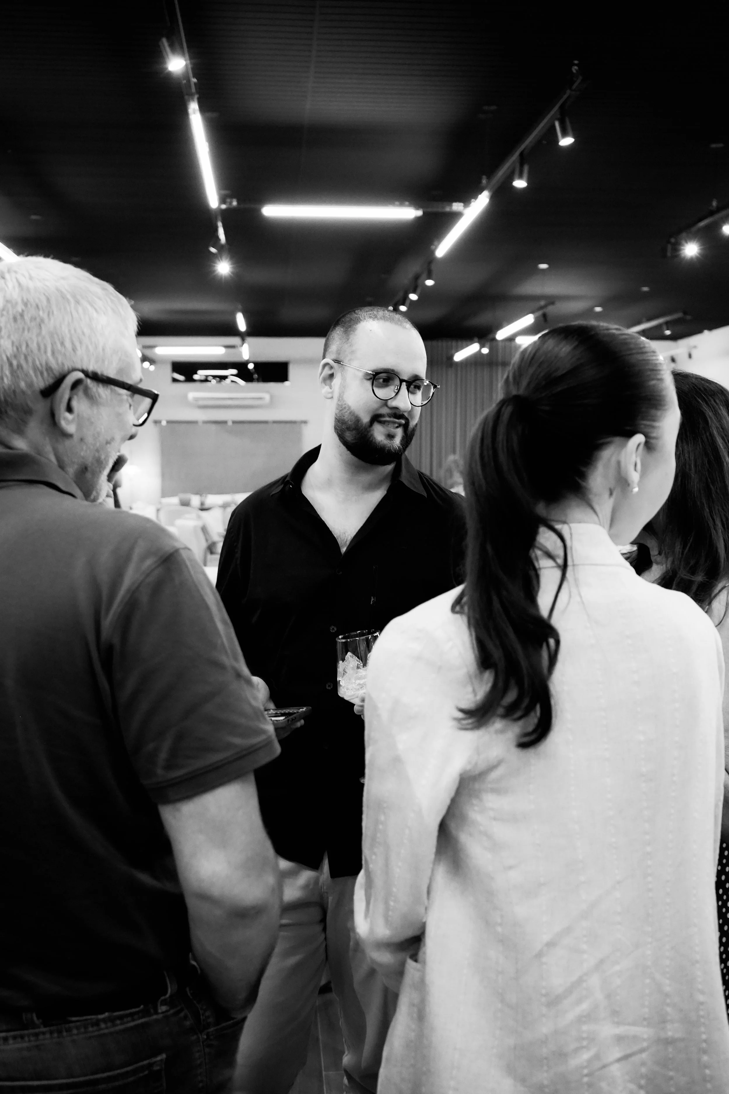 Homens e mulheres conversando em uma reunião social ou evento, ambiente interno com iluminação moderna.