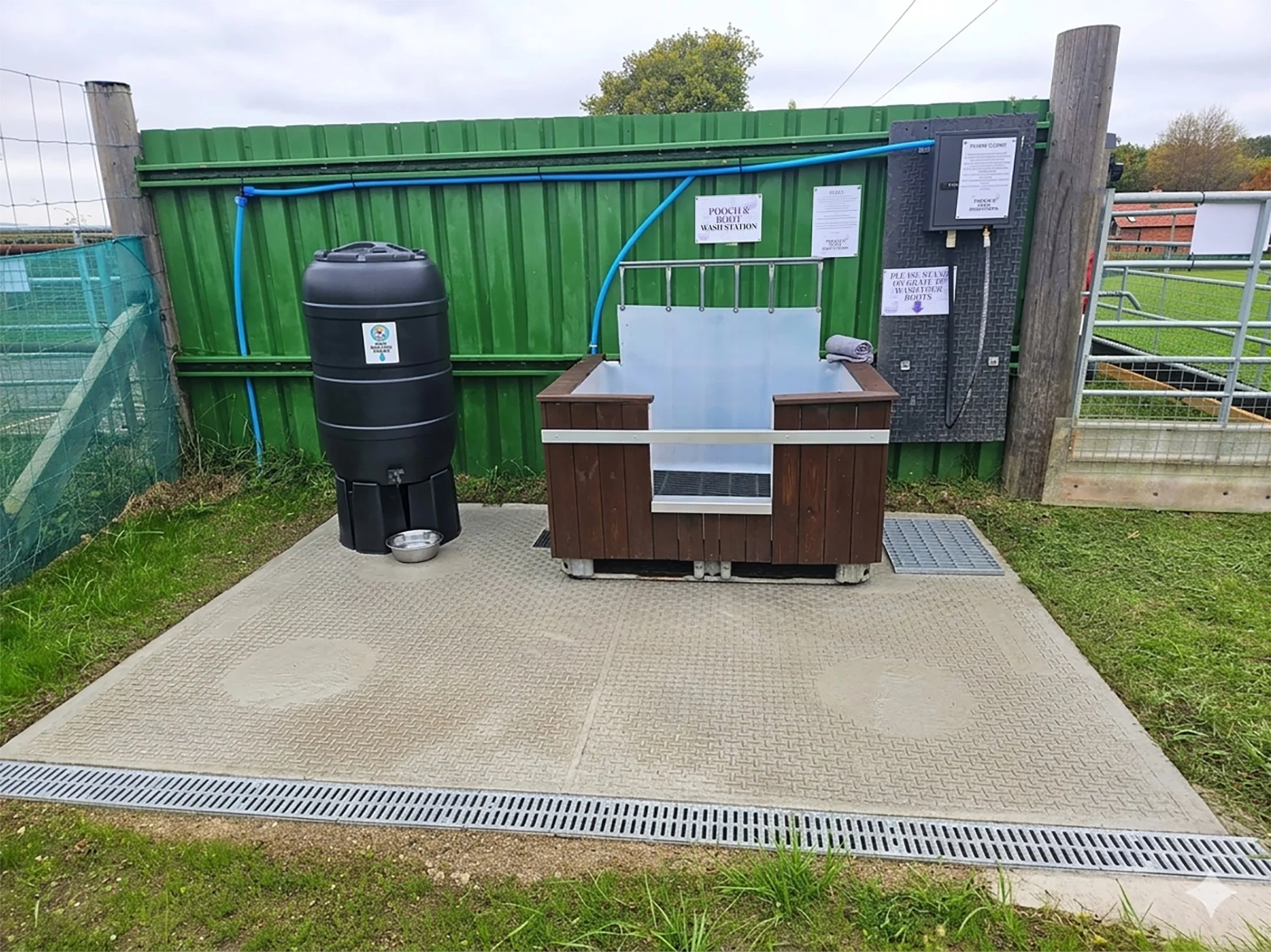Pet washing station with a water tank, wash basin, and grooming tools outside in a fenced area.