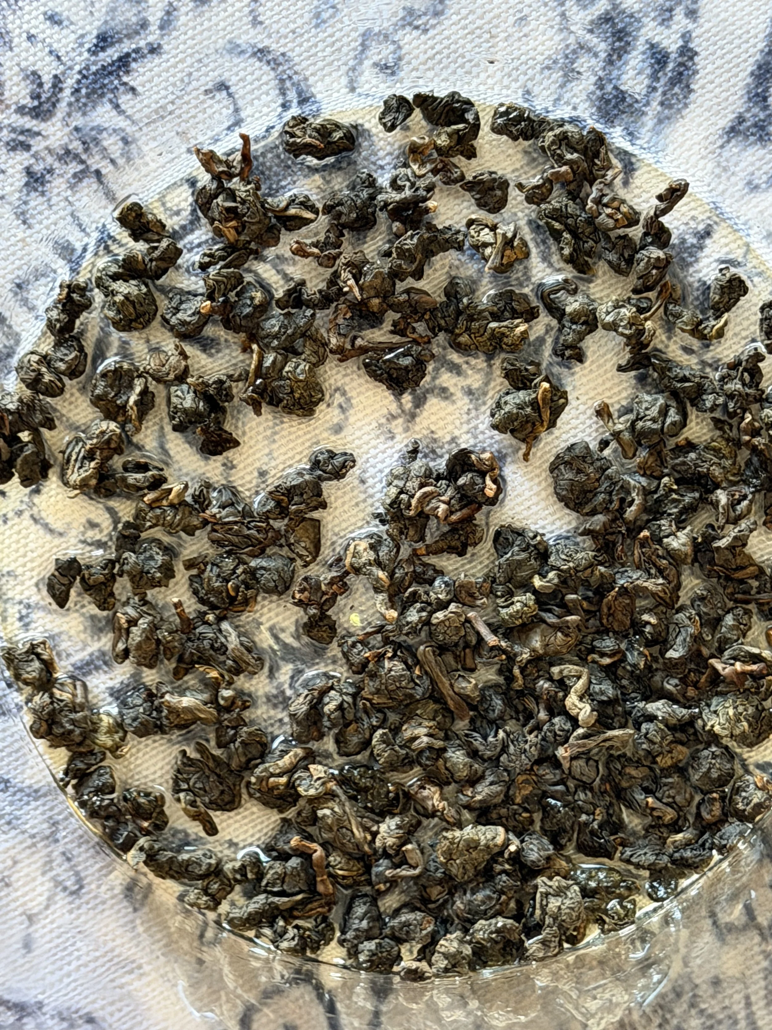 Tightly rolled dry Iron Goddess of Mercy oolong tea leaves spread across a light woven cloth.