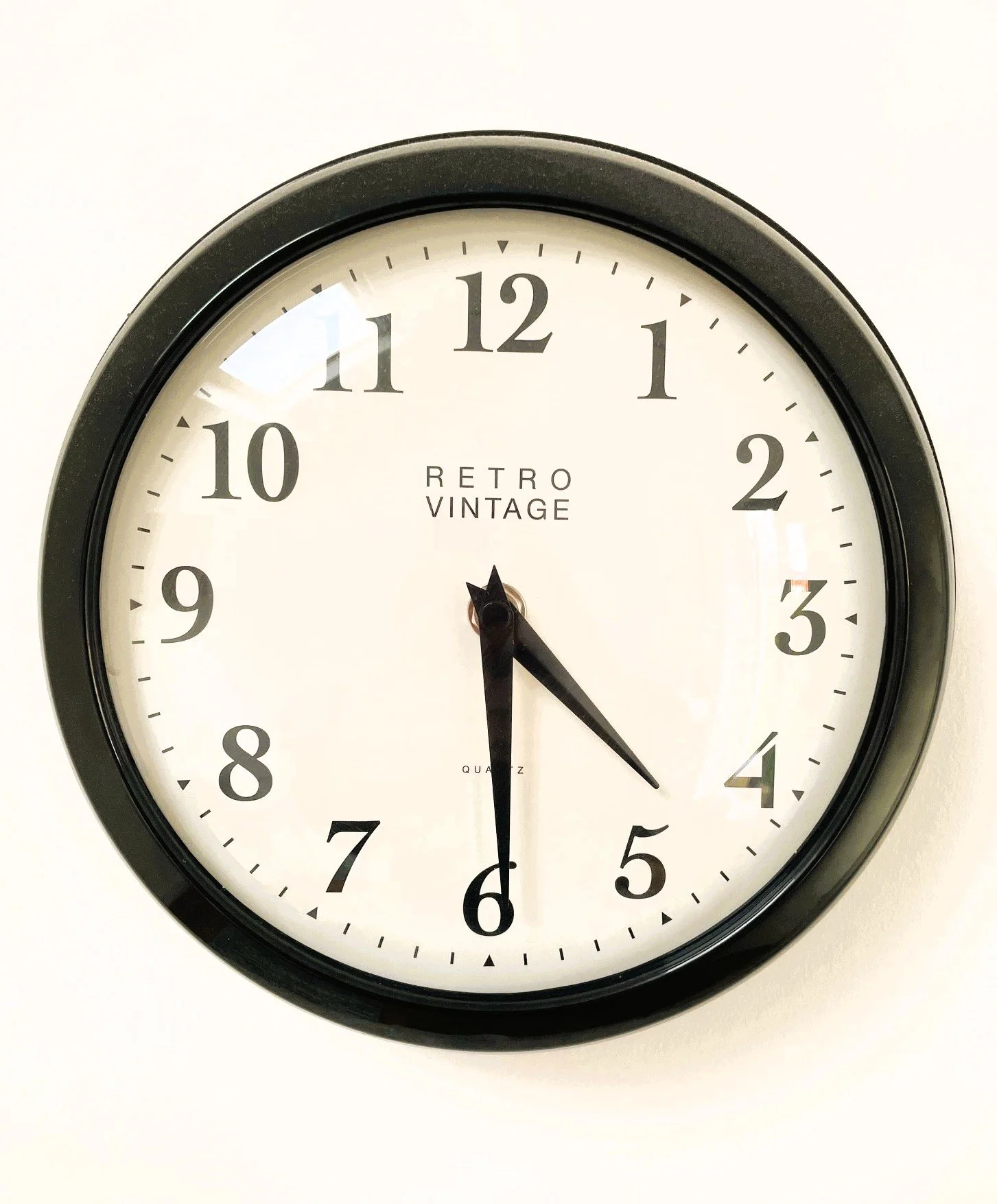 Black-framed wall clock showing 4:30 with white face and black numbers.