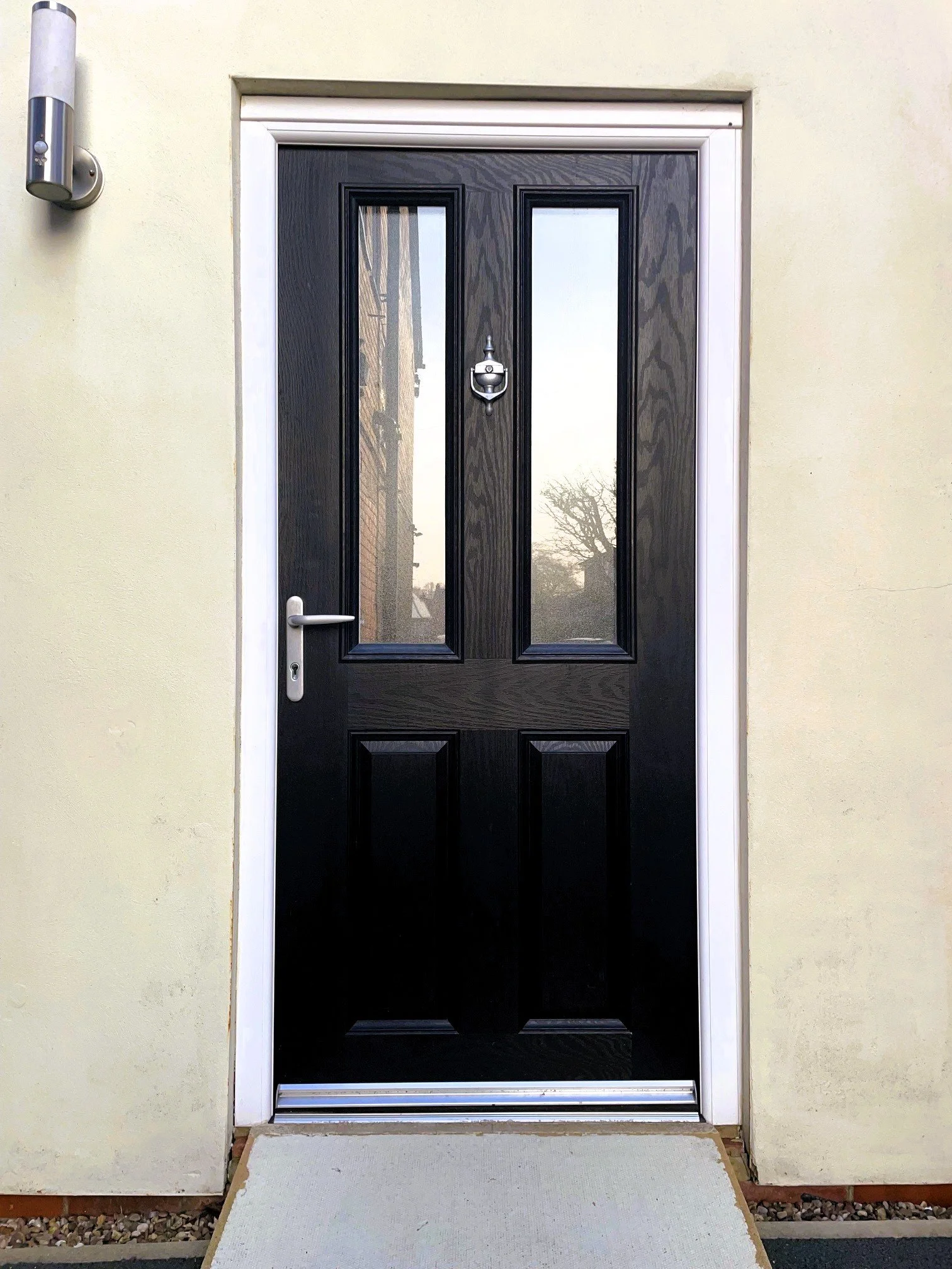 Black front door with two glass panels, white trim, silver handle, silver door knocker, and a small gray step in front.