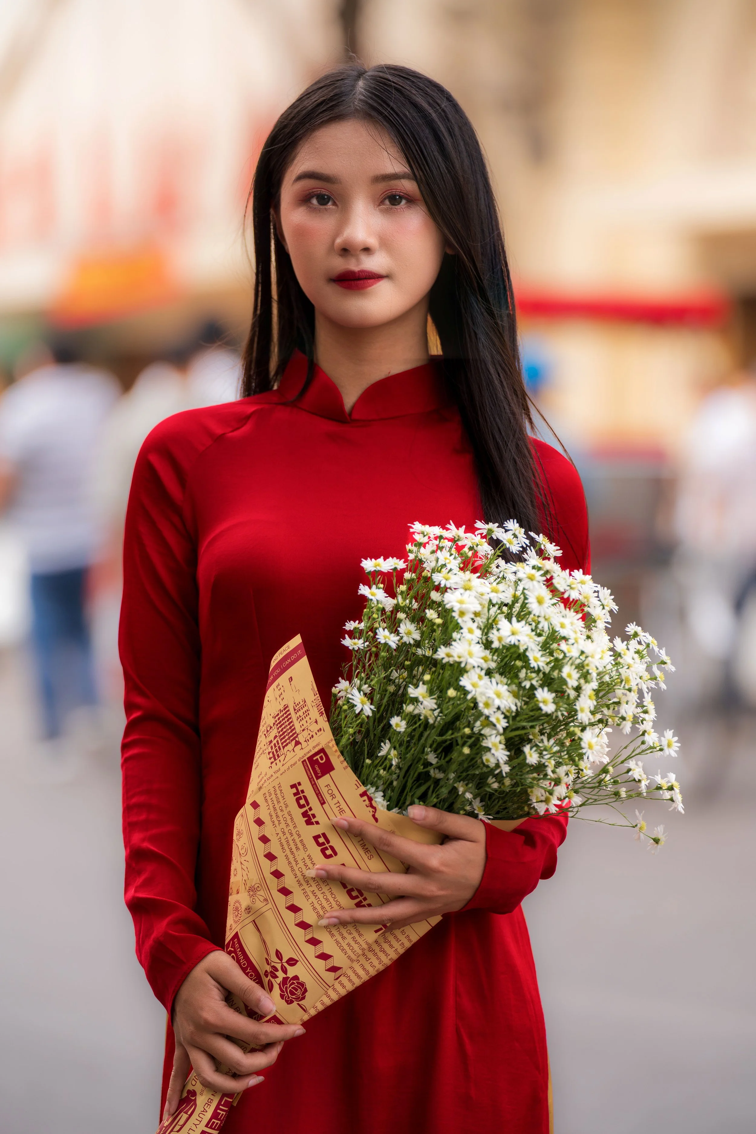 Vietnam - Una donna con abito rosso tiene un bouquet di fiori bianchi in una strada affollata.