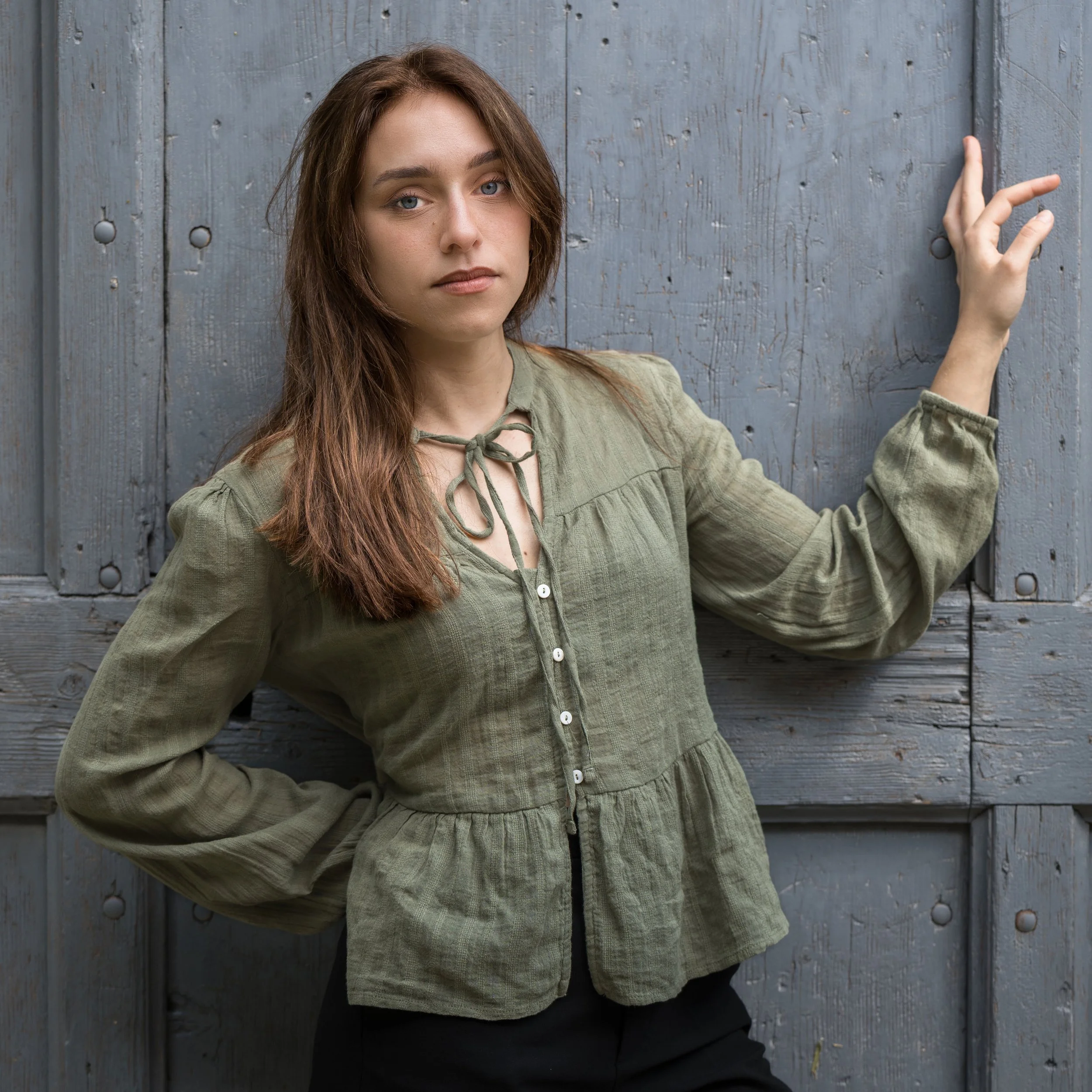 Chantal - Ragazza di fronte a una porta di legno azzurra, indossa una camicia verde e guarda verso l'obiettivo.