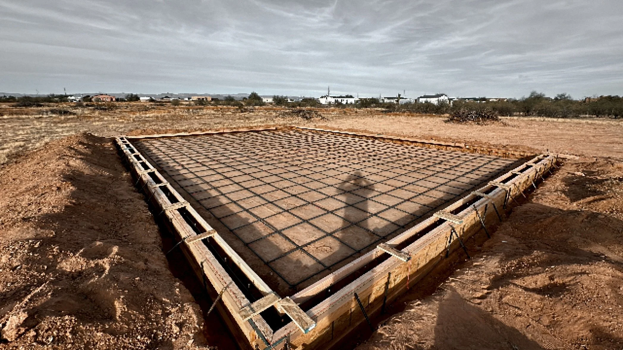 Construction site of a building foundation with wooden and metal framework in a desert landscape.