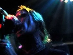 A singer performing on stage with dark lighting and colorful stage lights.
