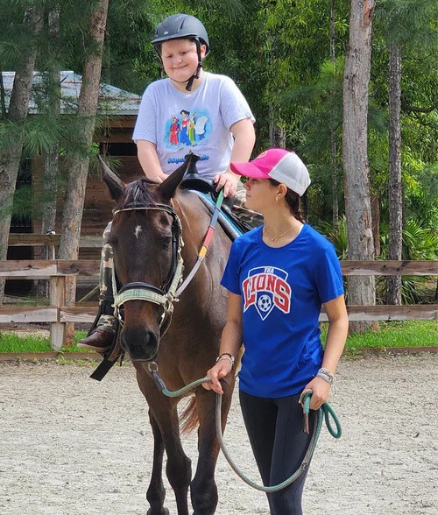 A boy riding a horse with a girl walking beside him holding the reins