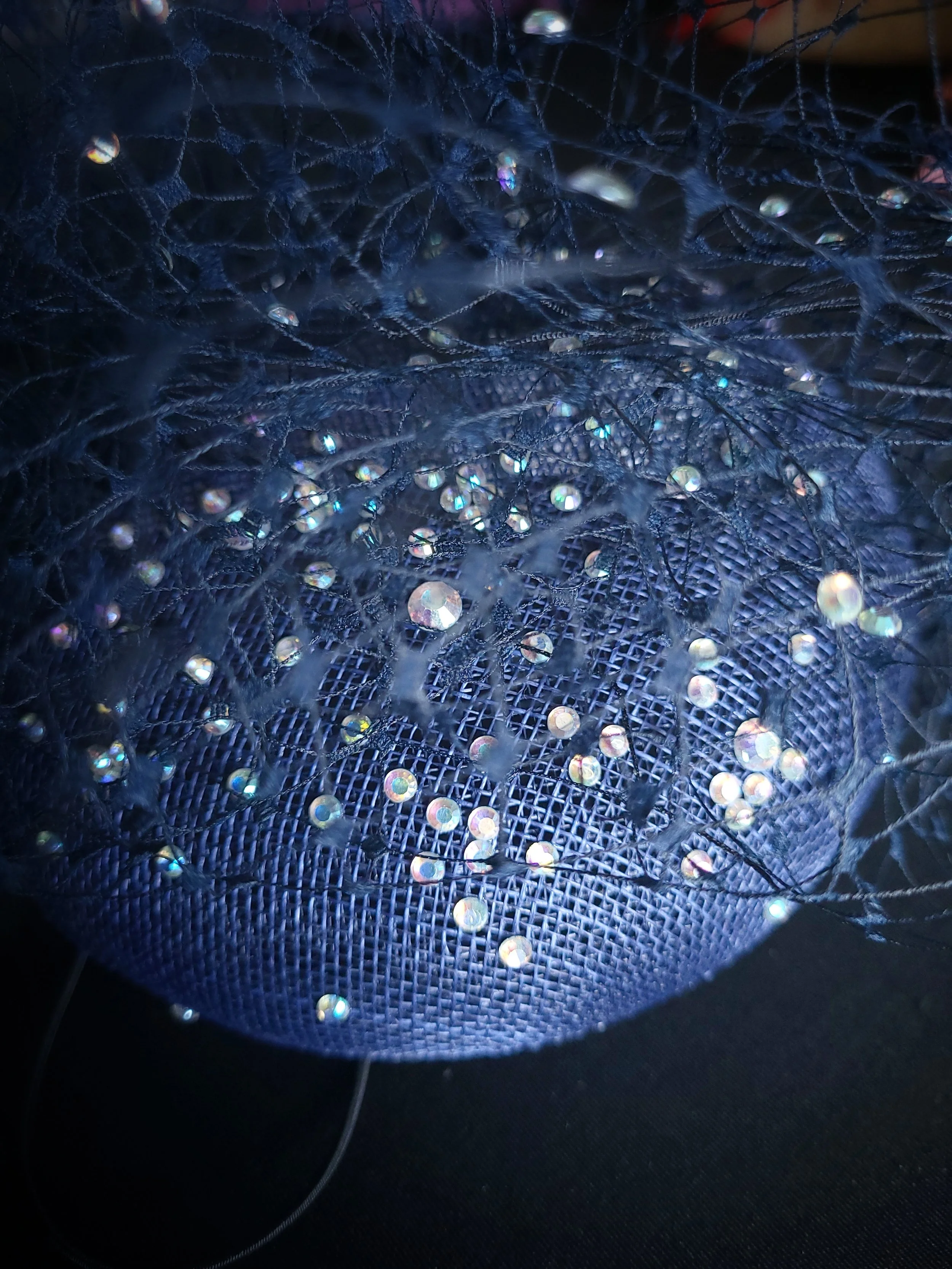 Close-up of a black wire mesh with small, bright, colorful lights or reflective decorations tangled on it.