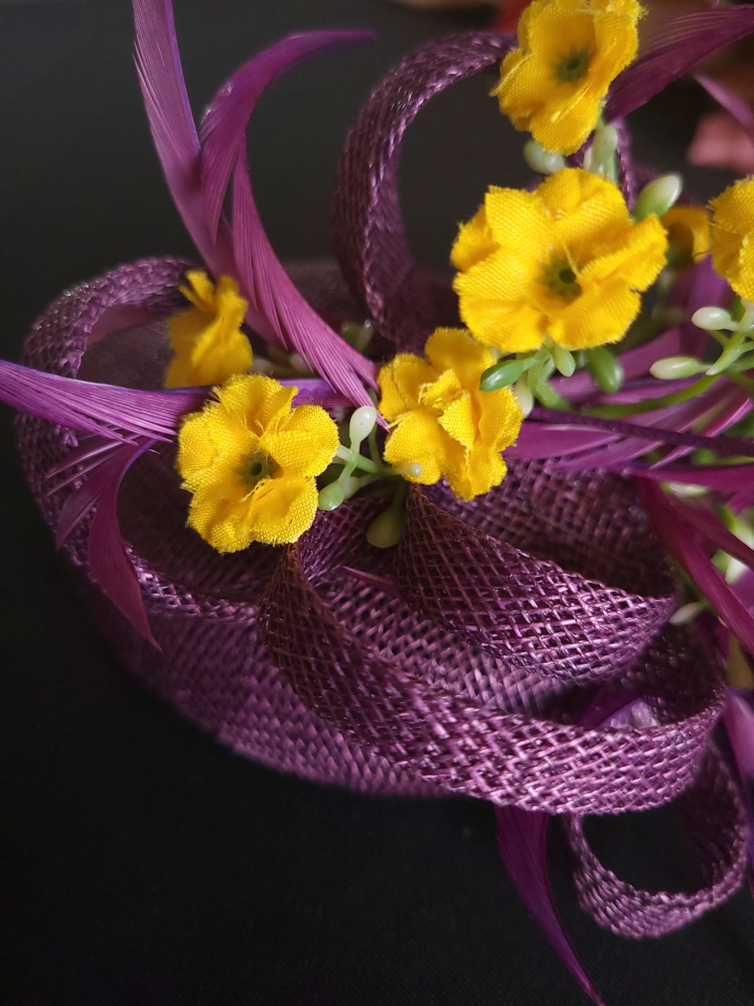 Close-up of a decorative floral arrangement with small yellow flowers, purple ribbon, and purple mesh material against a dark background.