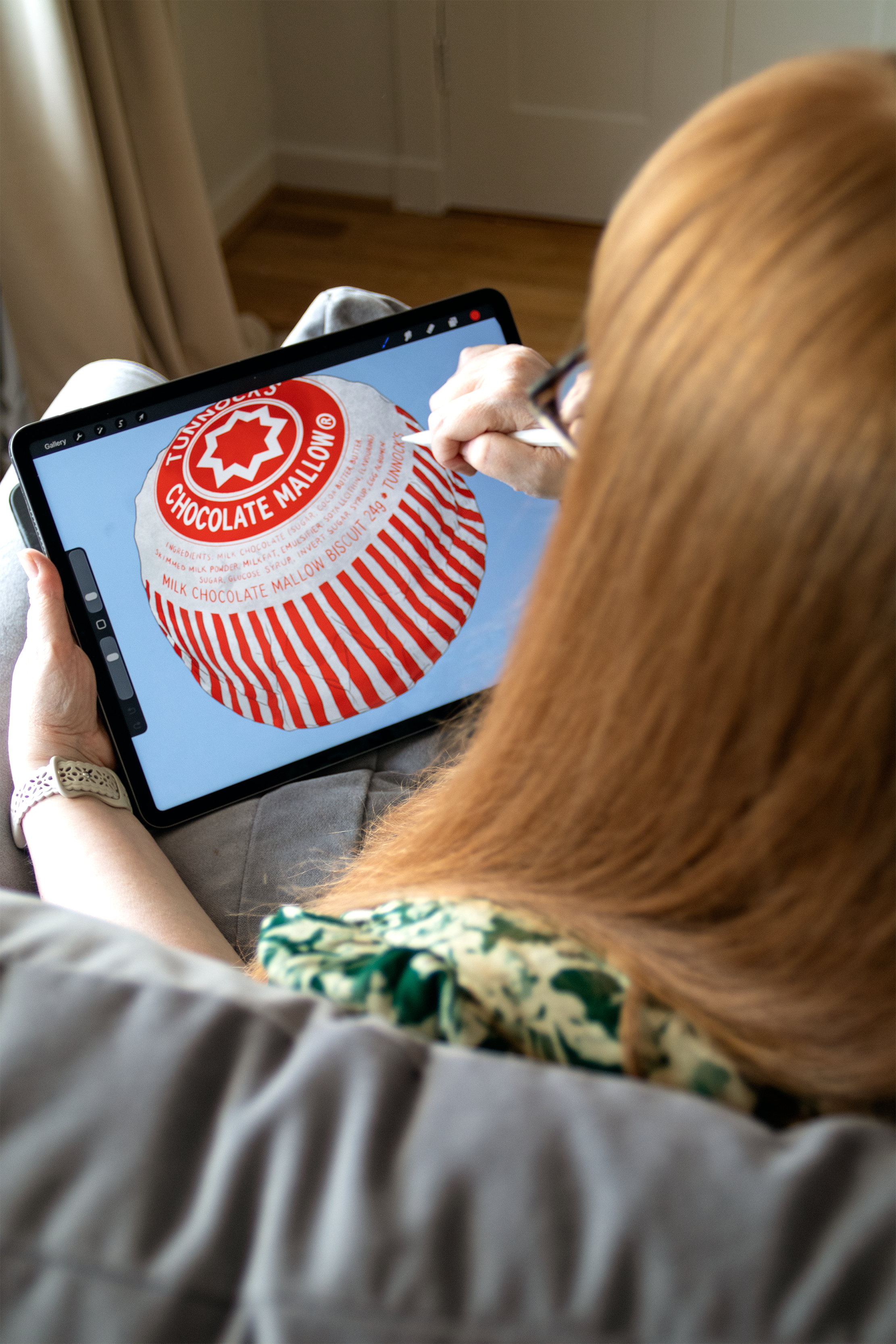 Photograph of a woman drawing on an iPad. The womand has long red hair and glasses.