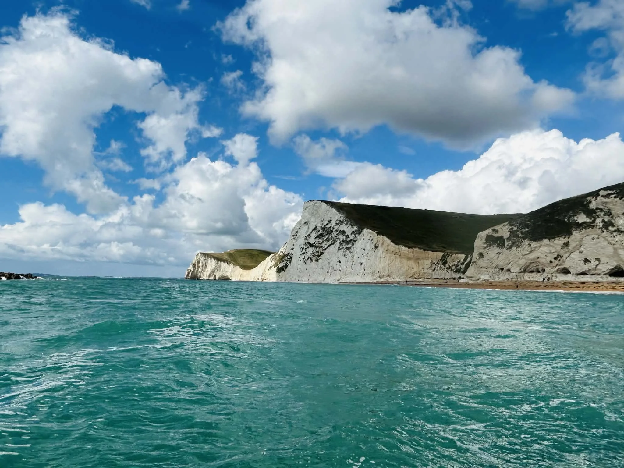 Scenic view of white chalk cliffs along the coast with turquoise water and a partly cloudy sky.