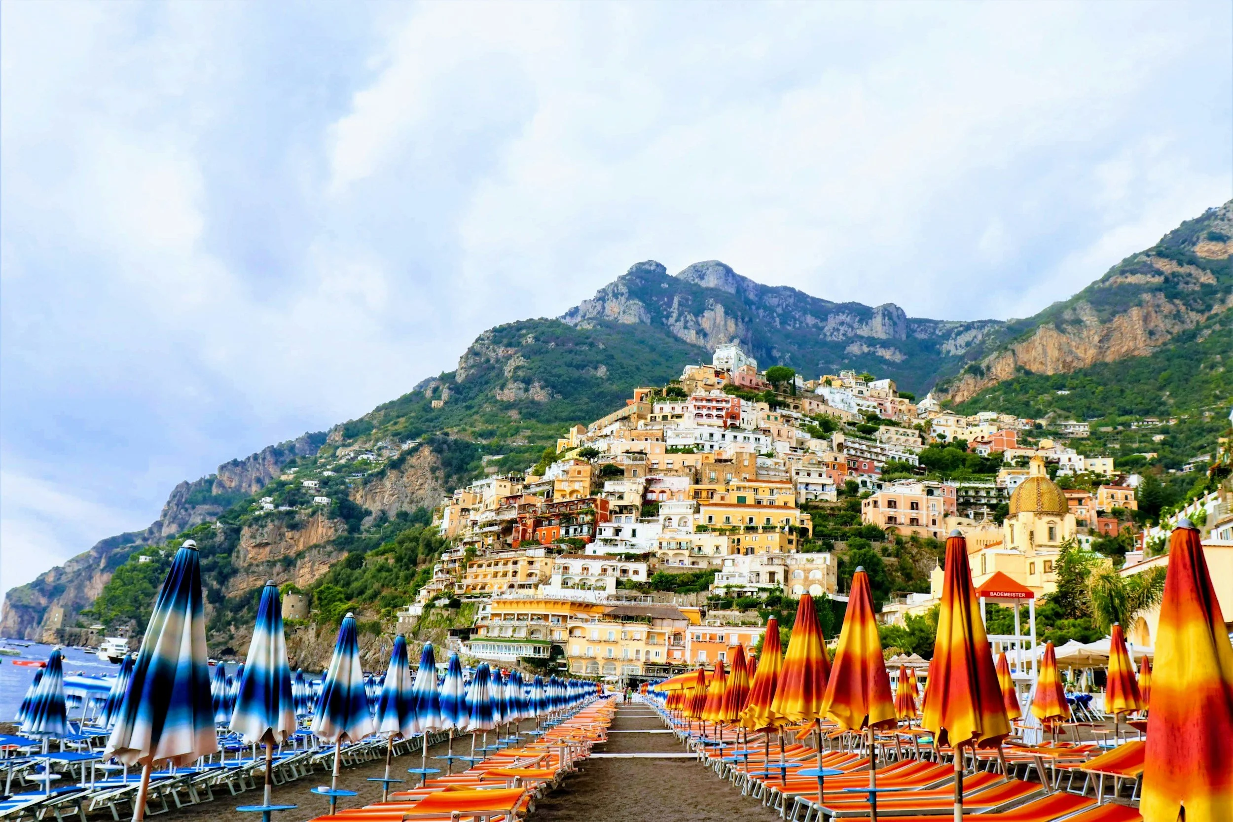 Colorful beach umbrellas and chairs on a sandy beach with a hillside town of colorful buildings in the background
