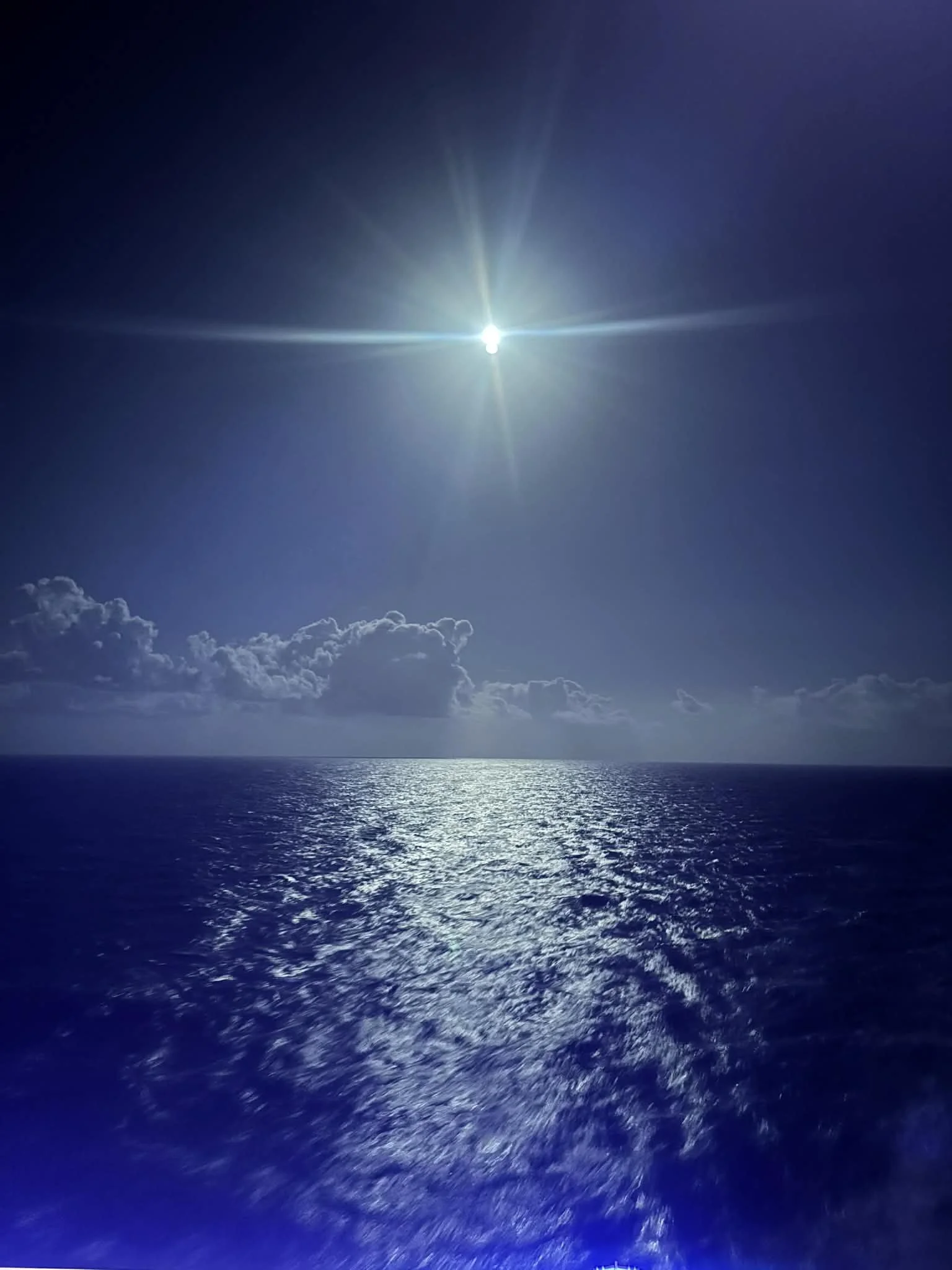 Bright sun shining over the ocean with reflection on the water and a few scattered clouds in the sky.