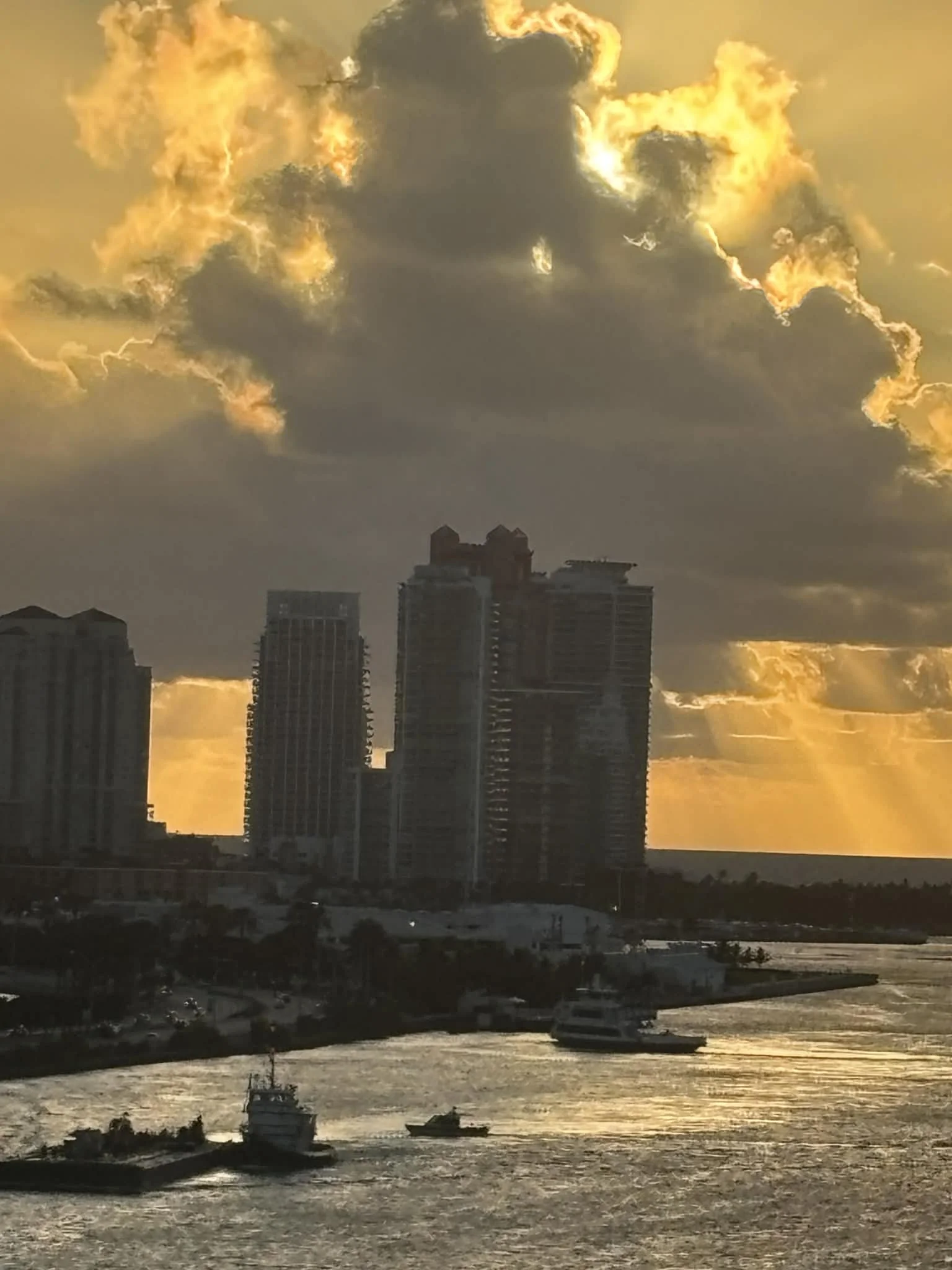 City skyline during sunset with tall buildings and a dramatic cloud-filled sky, with sun rays peeking through