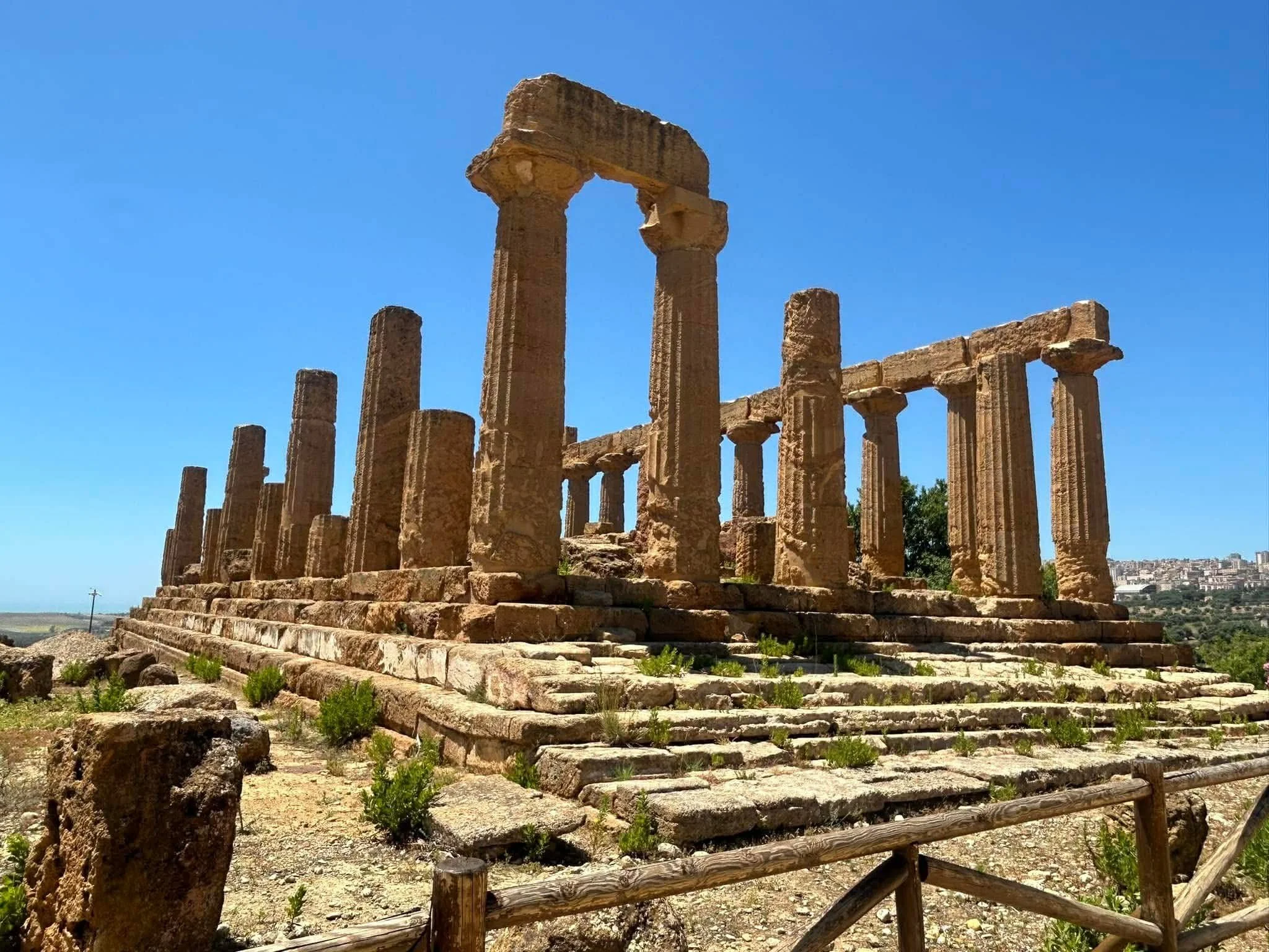 Ancient Greek ruins with large stone columns on a stepped platform against a blue sky.