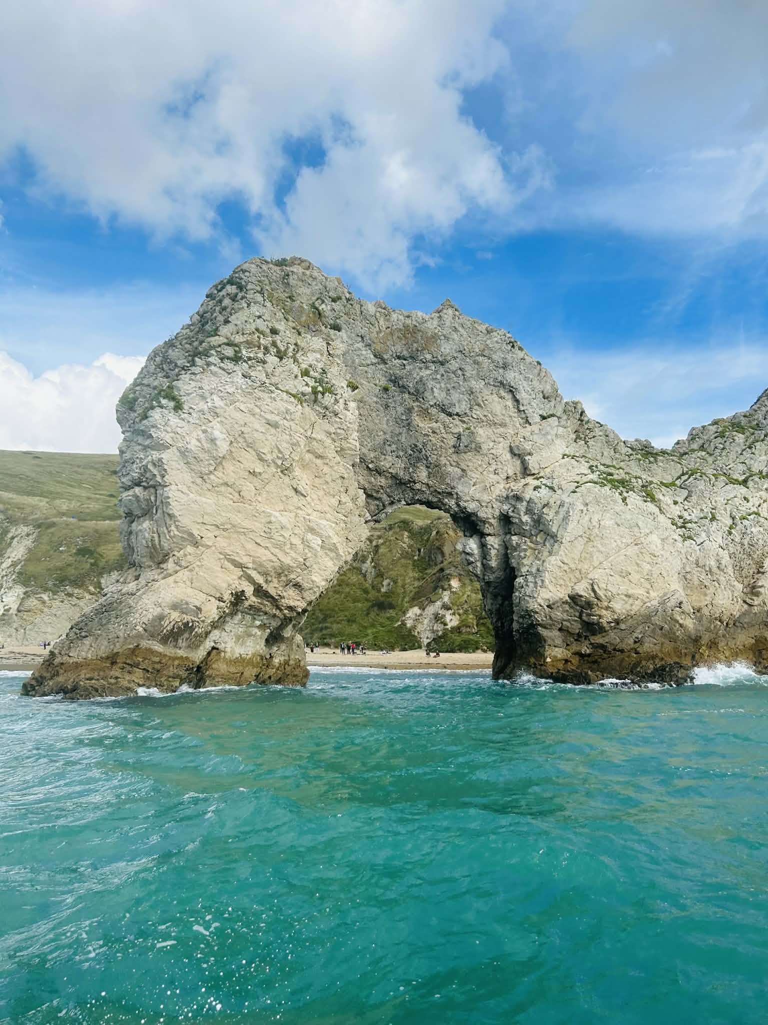 Natural arch rock formation on a shoreline with turquoise water and a partly cloudy sky.