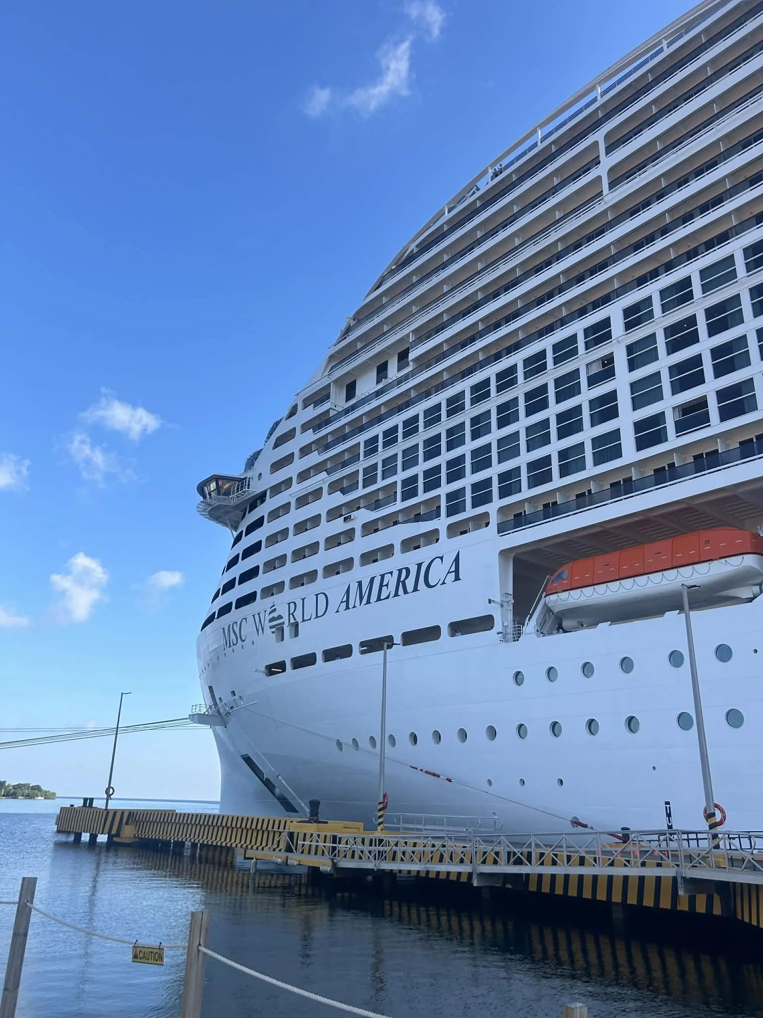 A large white cruise ship named MSC World America docked at a port with a clear blue sky above.