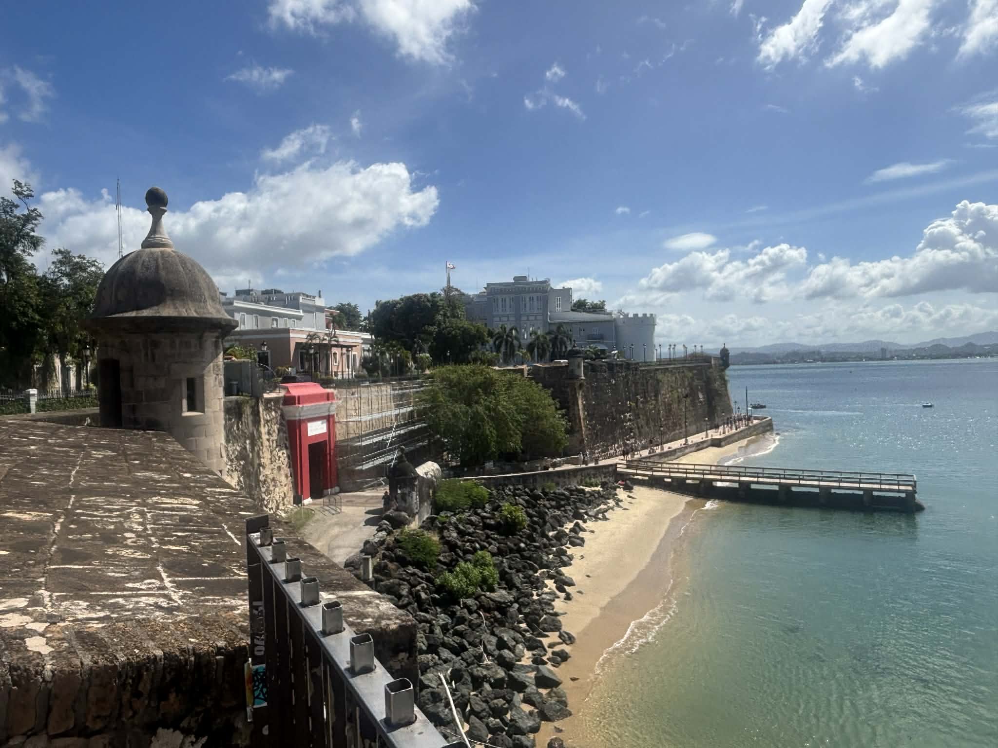 Sunny day at a historic fort overlooking a beach, with calm water and a partly cloudy sky.