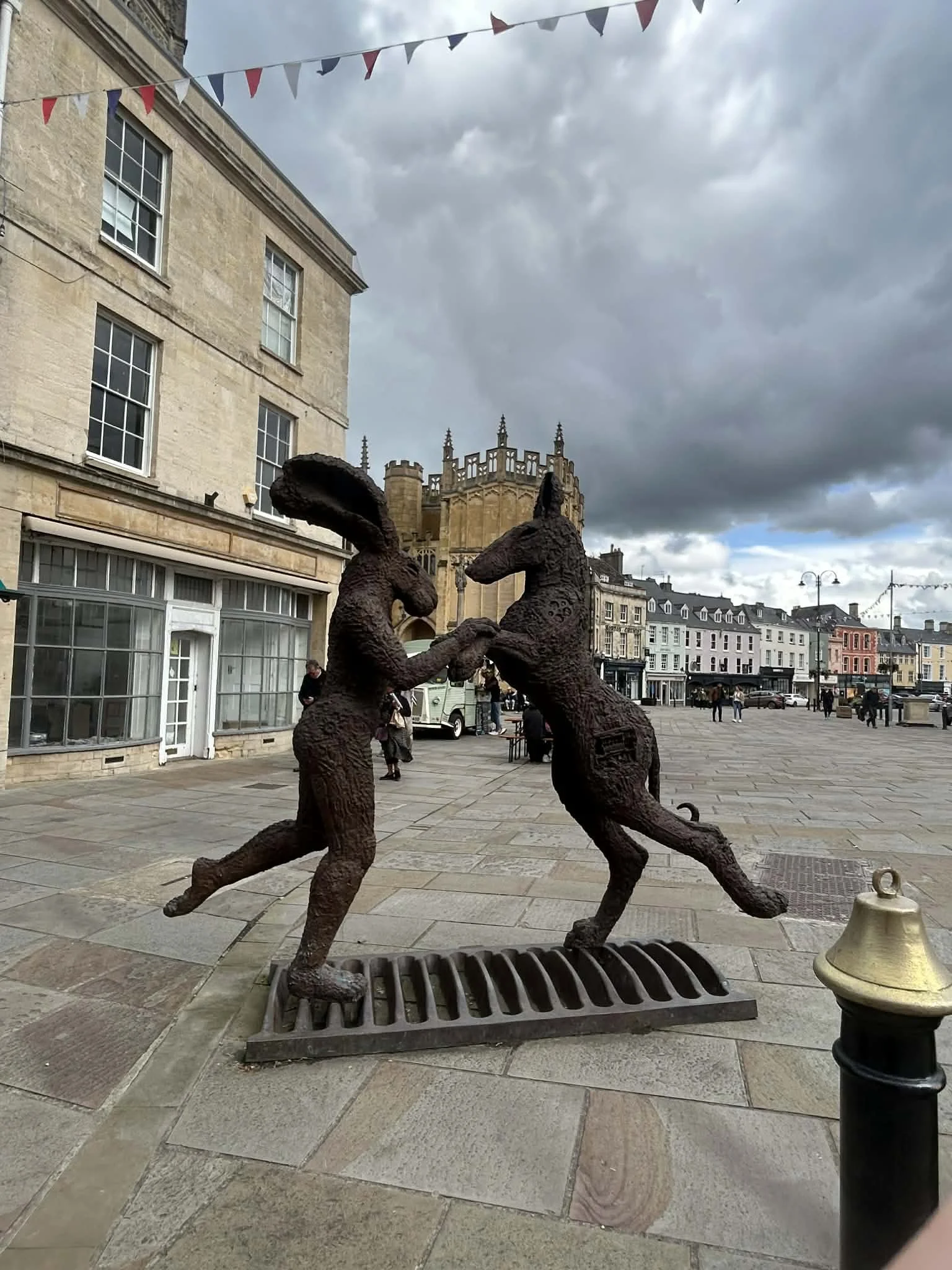 Bronze sculpture of two kangaroos standing on hind legs and holding each other's paws, located on a city street with historic buildings and cloudy sky in the background.