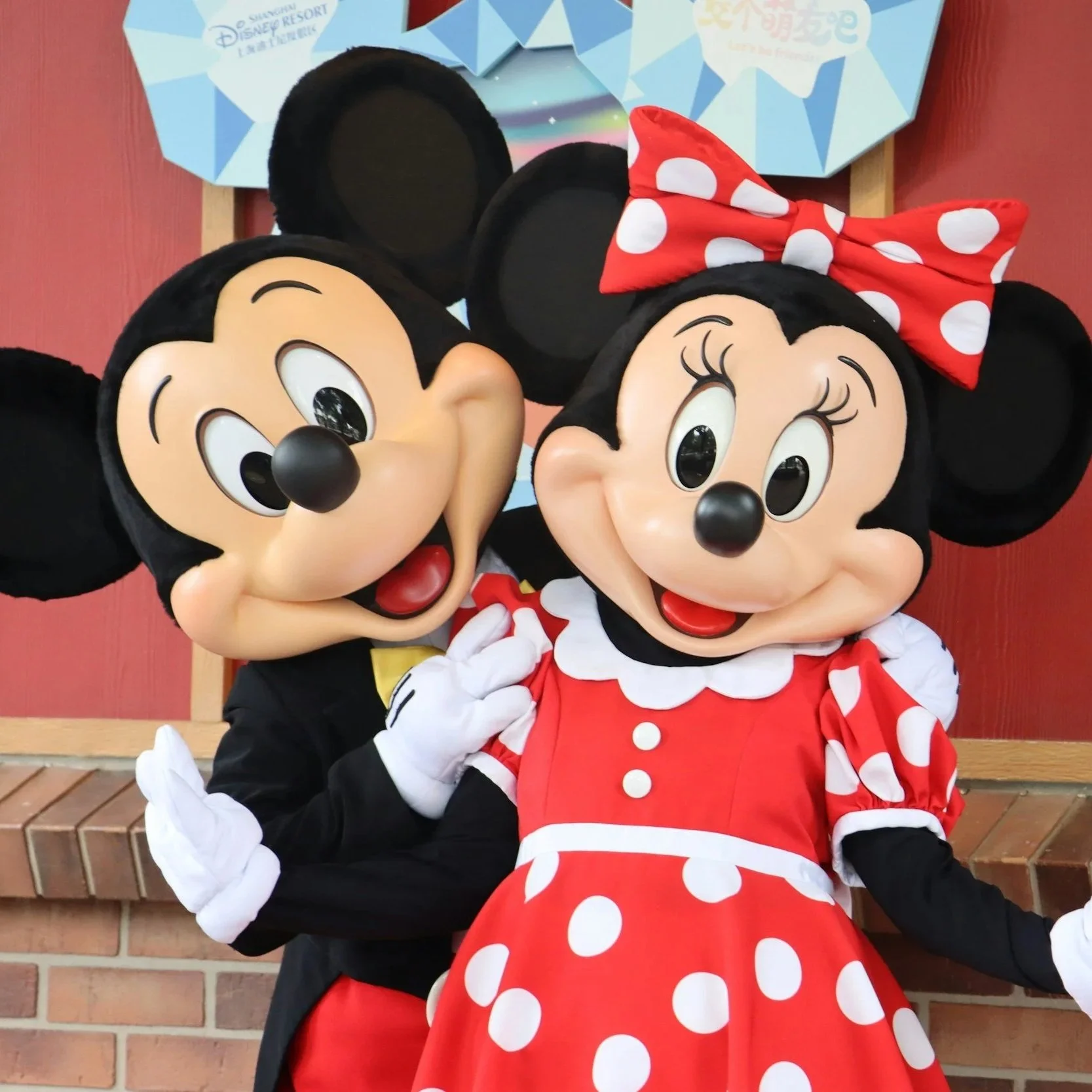 Costumed characters of Mickey Mouse and Minnie Mouse dressed in red and white polka dot outfits, standing in front of a Disney sign.
