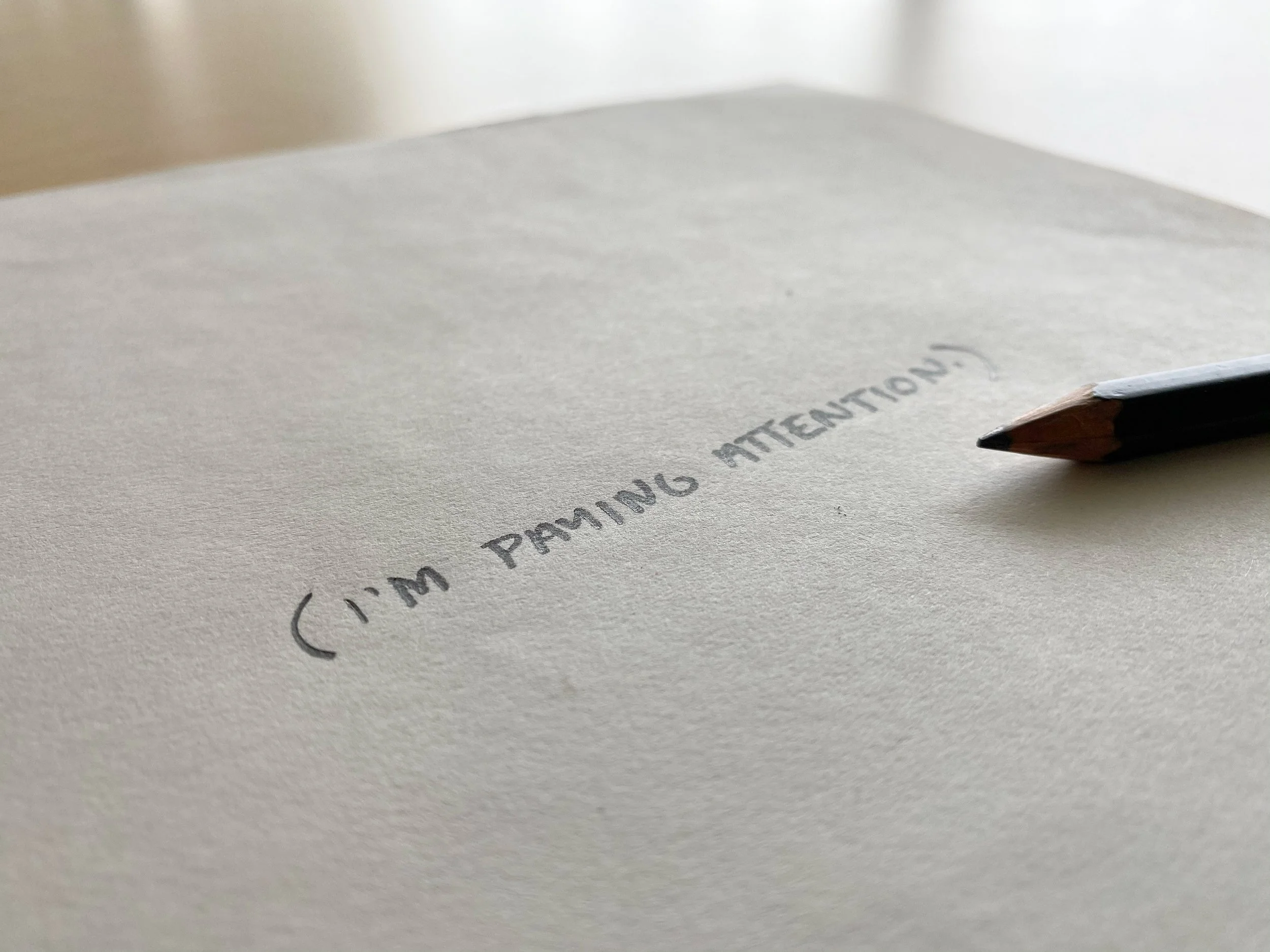 Close-up of a pencil writing on a piece of paper with partially visible text.