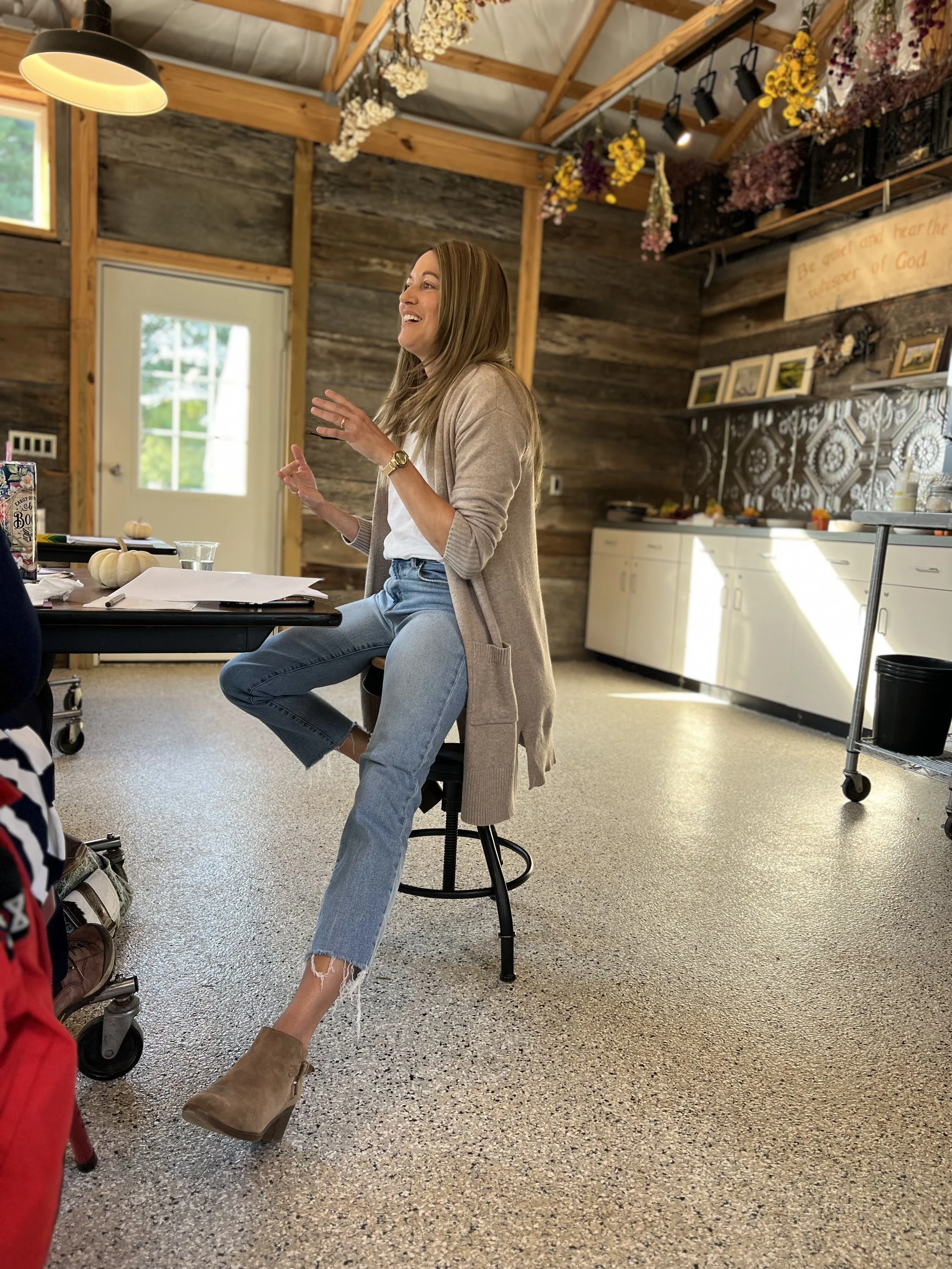 Author Julie Yost sitting on a stool, speaking to a group at a women's retreat in a cozy, rustic room.