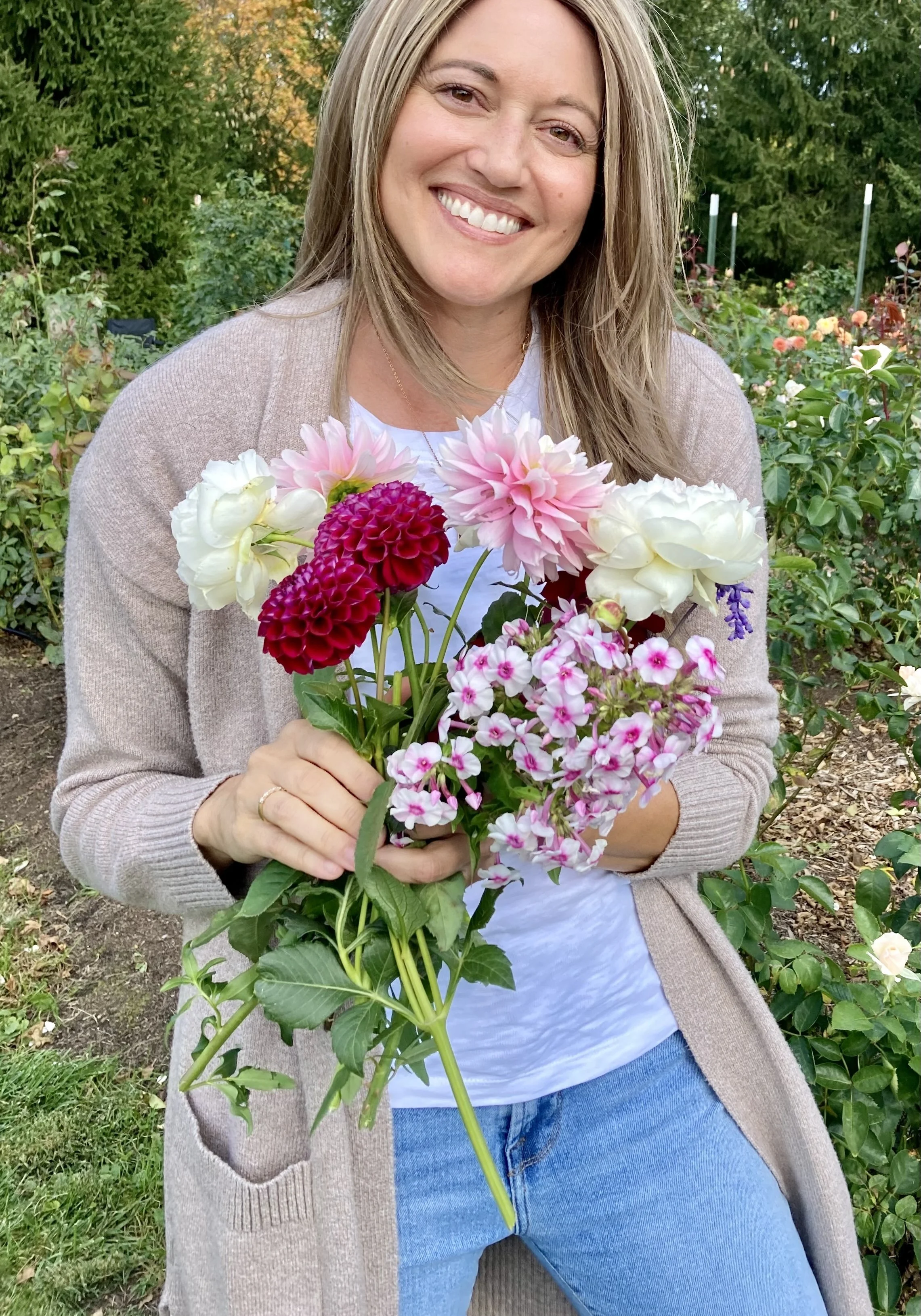 Author Julie Yost smiling while holding a colorful bouquet of flowers in a garden.