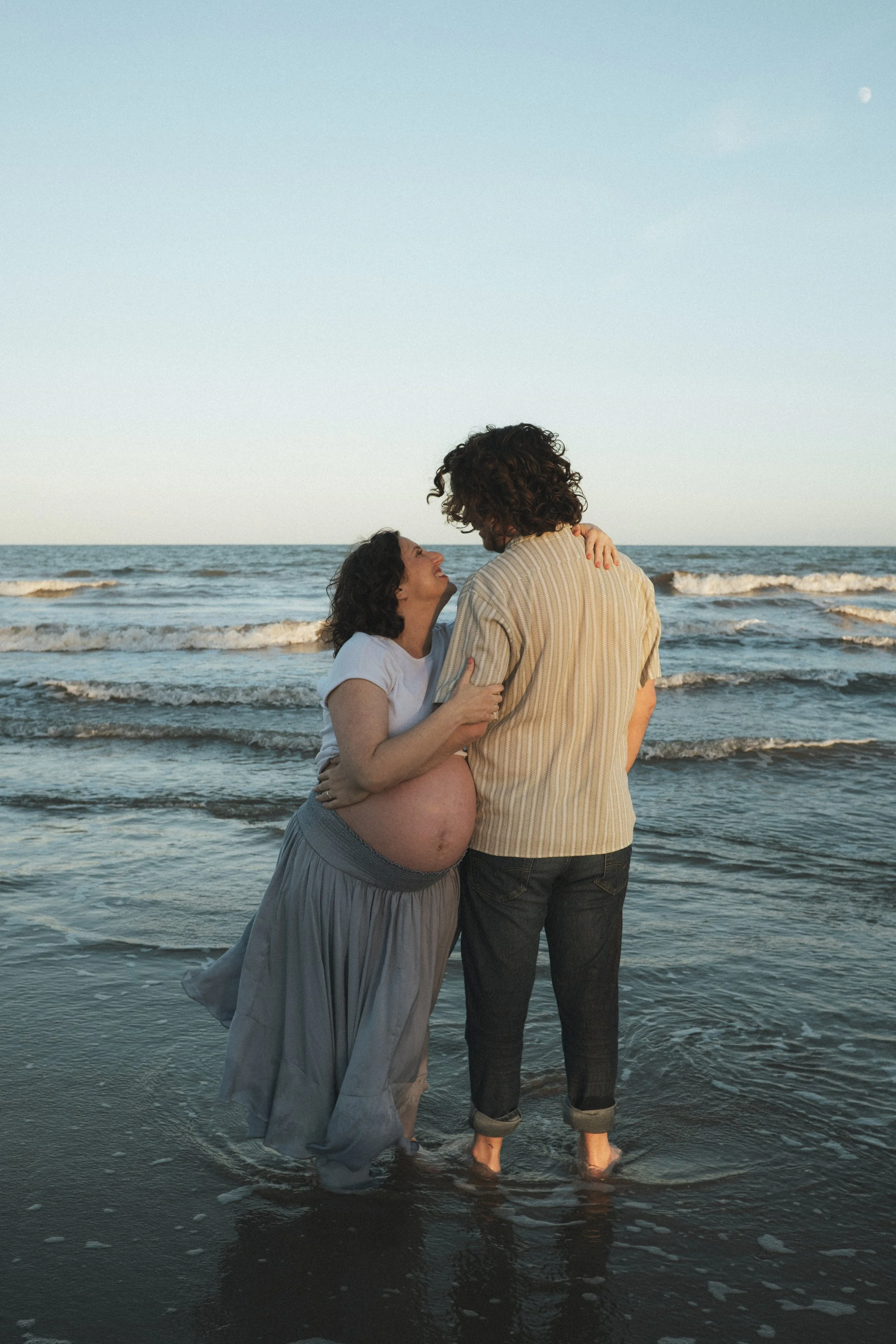 Pregnant couple embracing in shallow ocean water at the beach