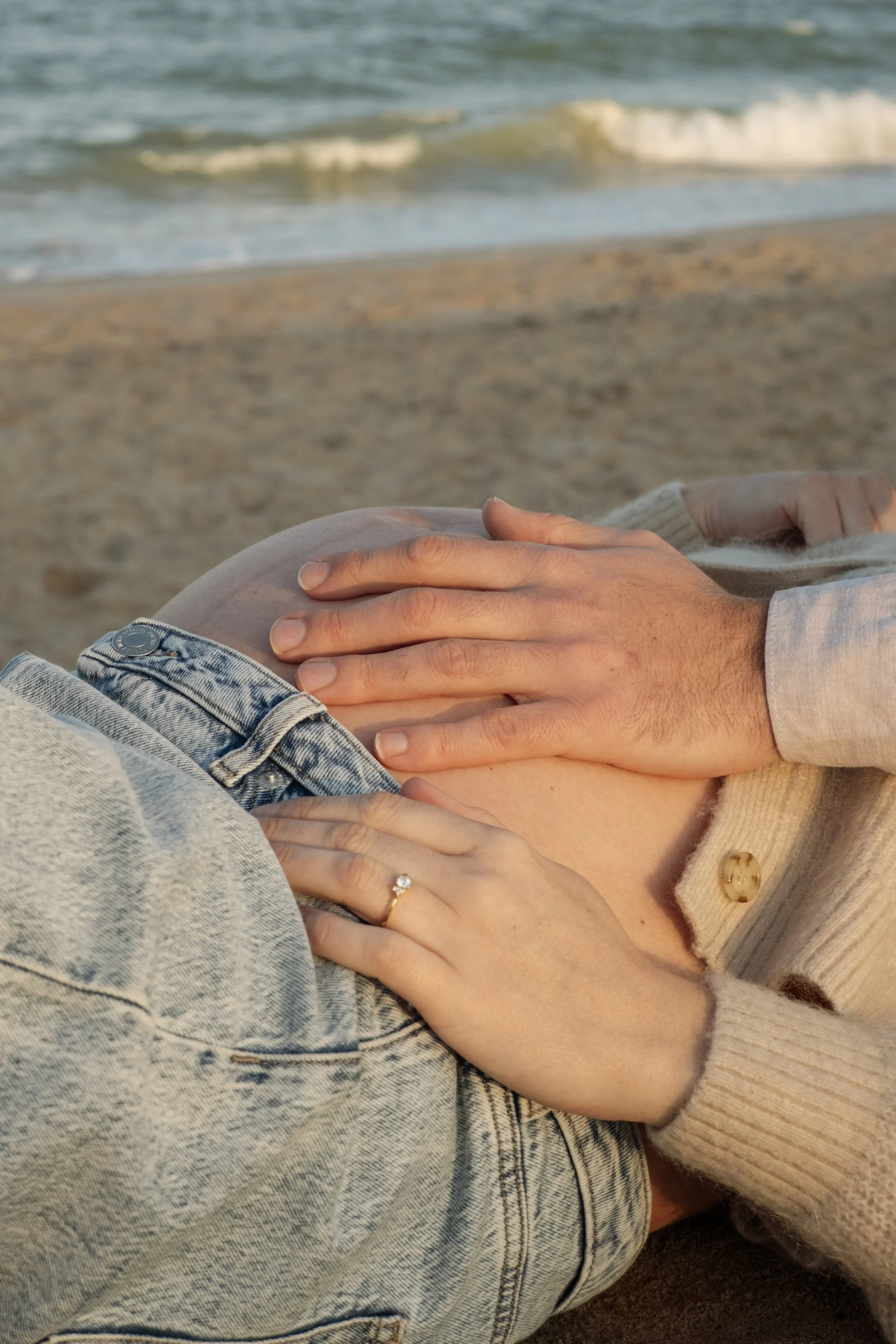 Close-up of a couple embracing on the beach, focusing on their hands and torsos with the ocean in the background.