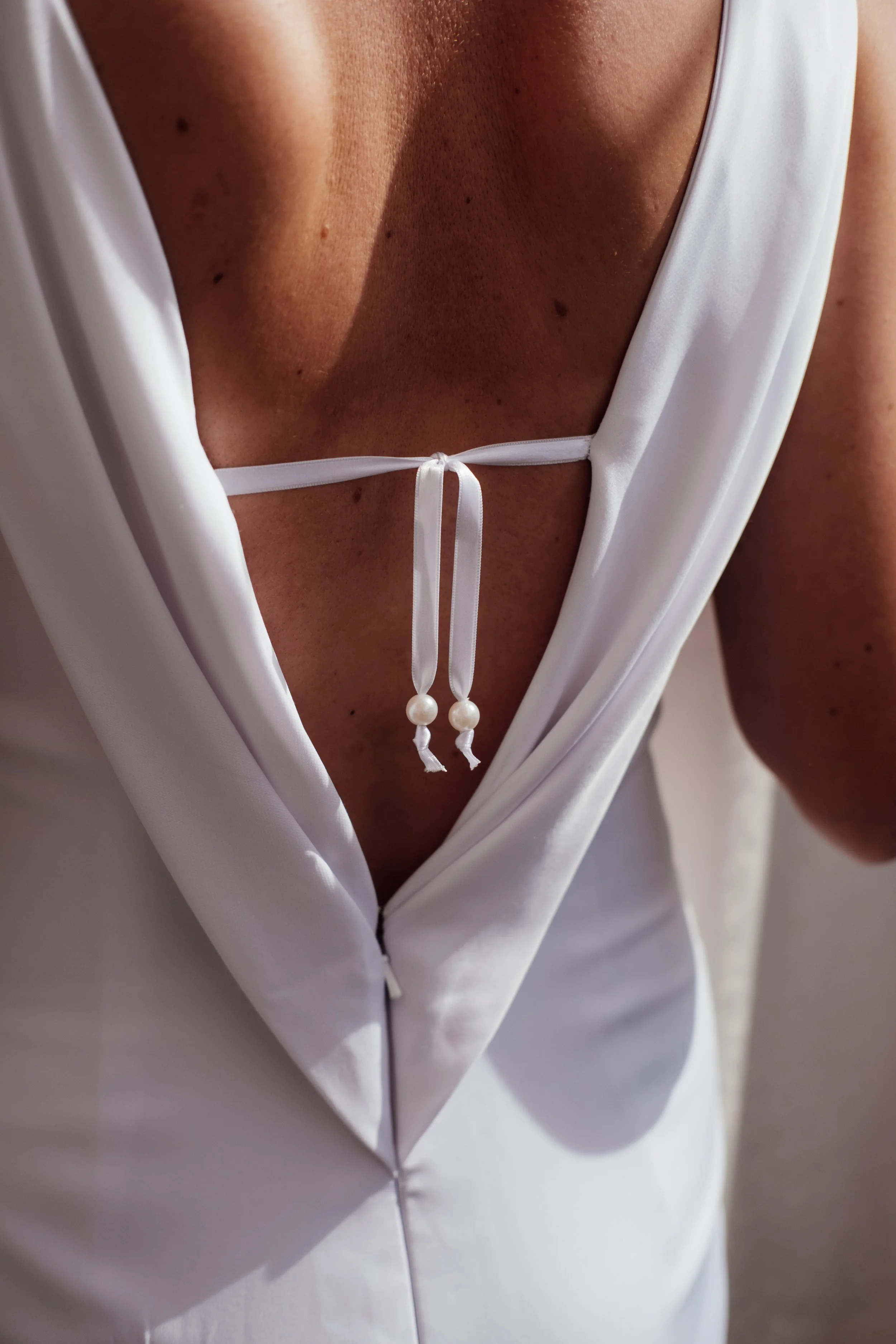 Close-up of a woman’s chest and lower face, showing a white V-neck top tied with a small string and beads, with a plain background.