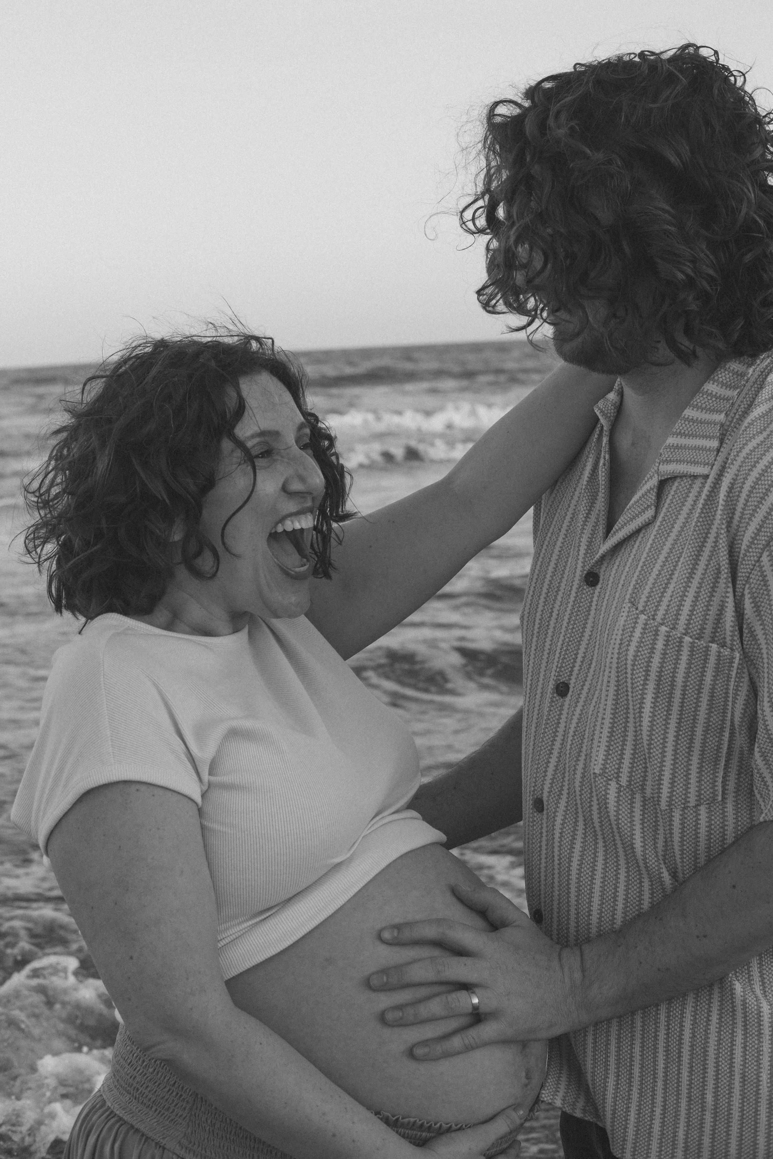 Black-and-white photo of a smiling couple embracing beside the ocean.