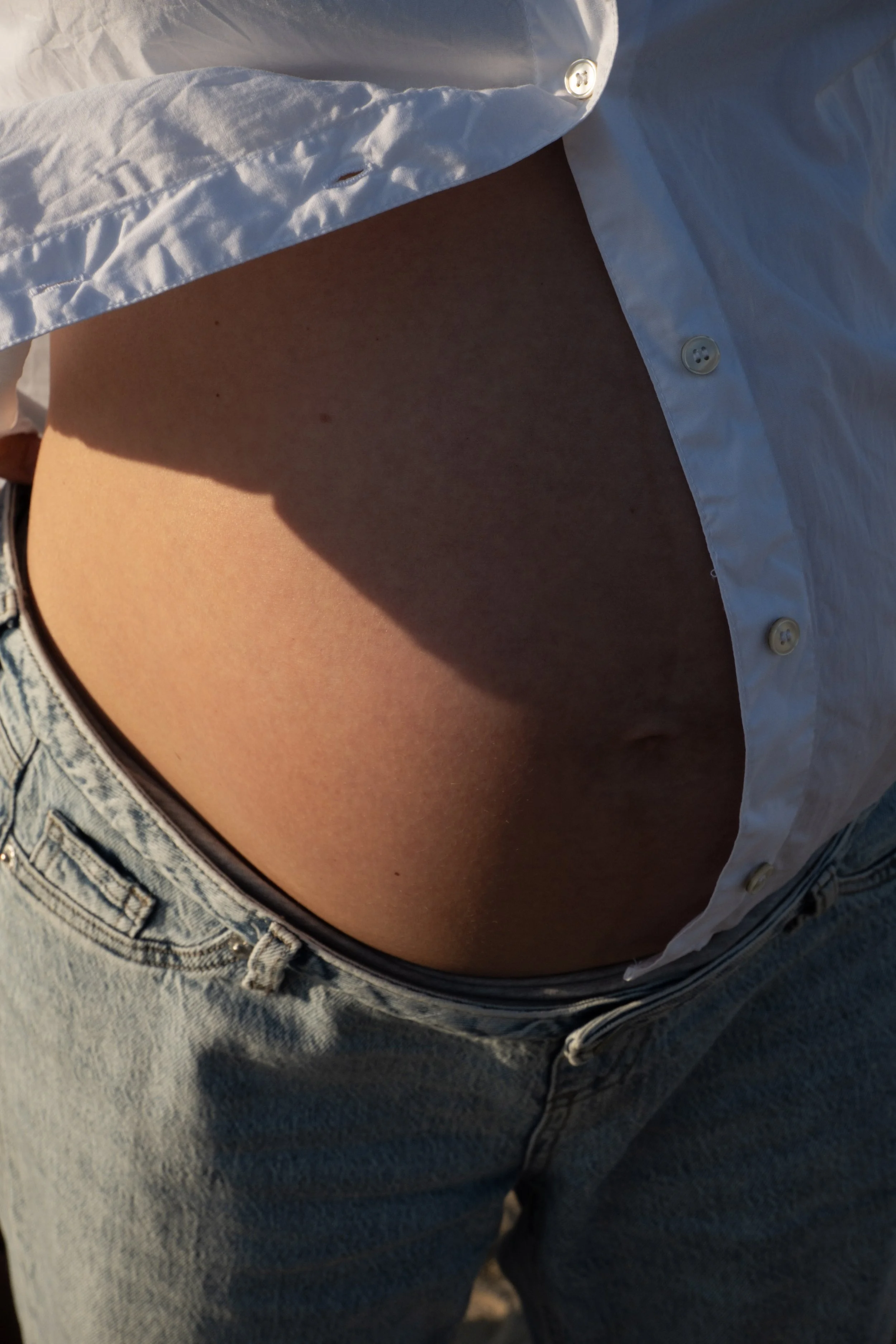 Close-up of a person wearing a partially unbuttoned white shirt and high-waisted blue jeans.