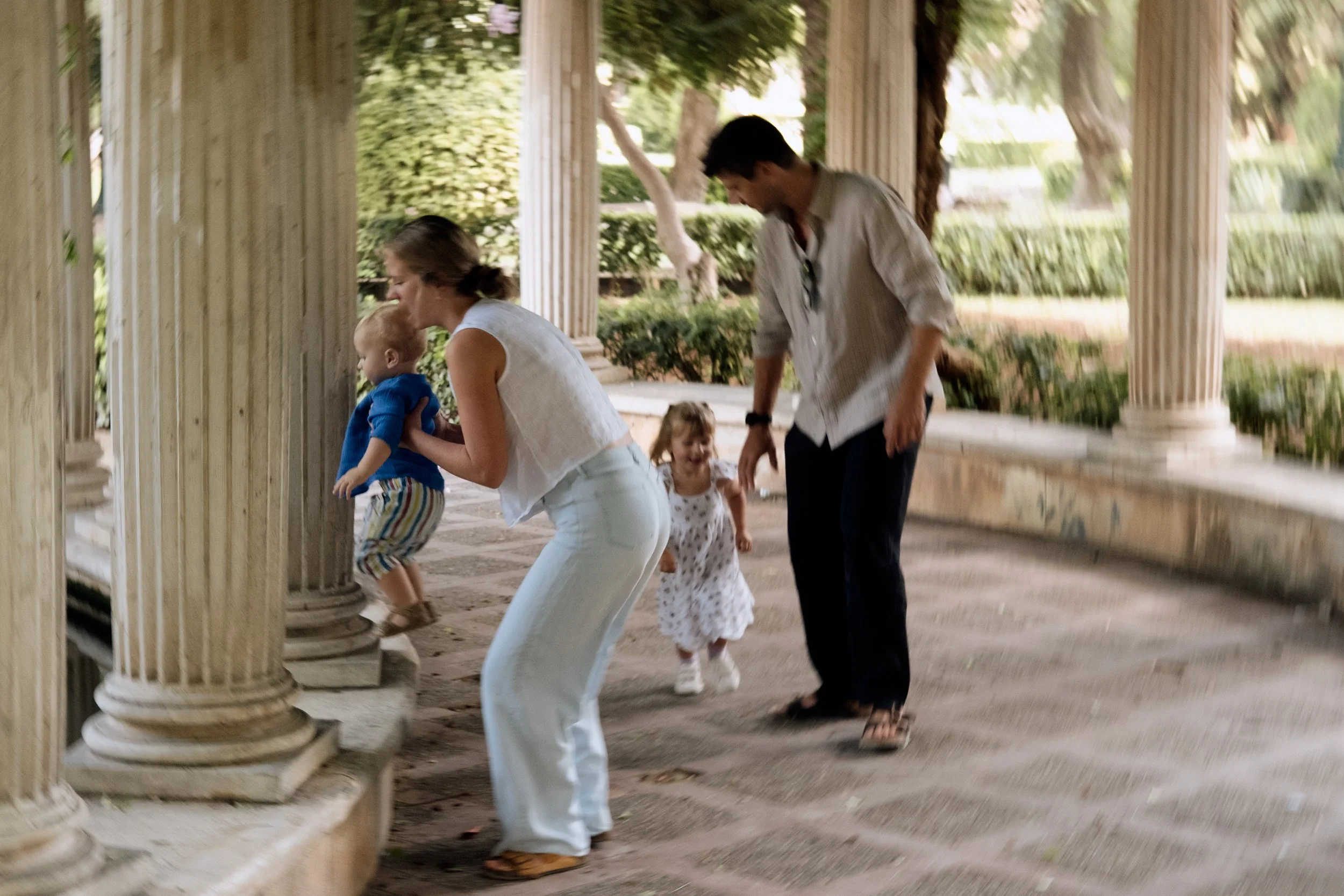 Family with two children playing on ancient Greek-style columns in a park or historical site