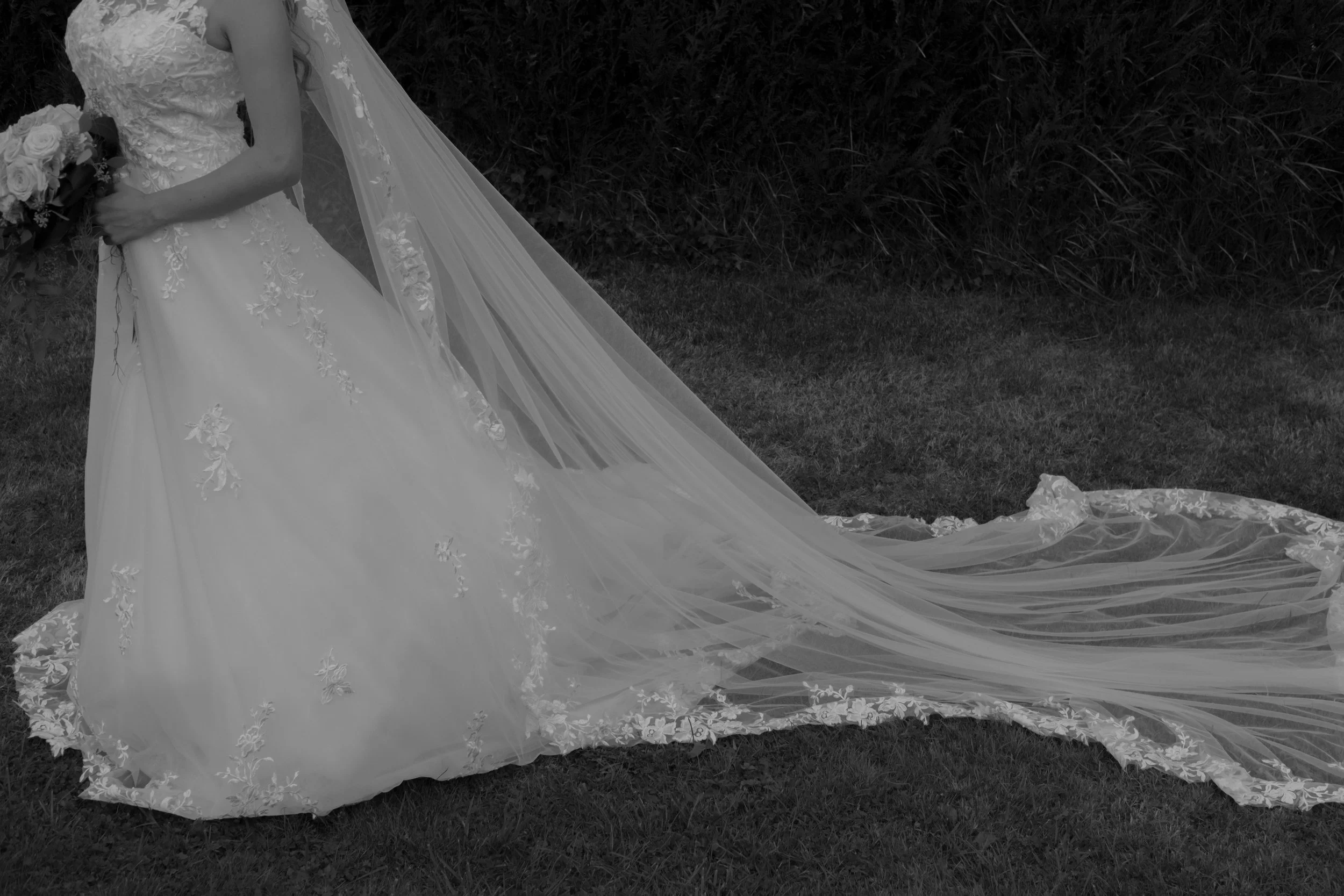 A bride in a wedding dress holding a bouquet standing on grass with her long train spread out behind her.