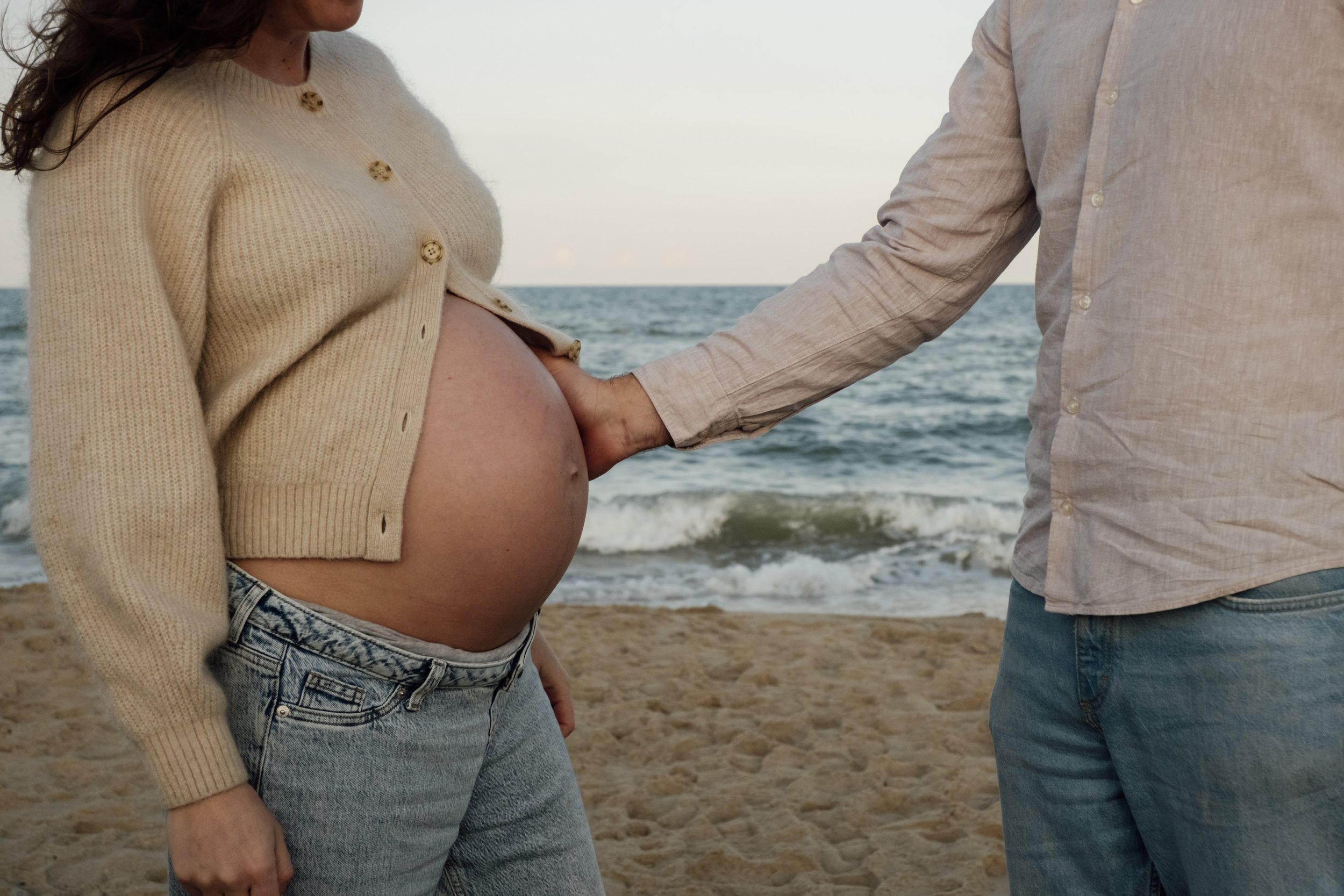 A pregnant woman and a man holding hands on a beach.