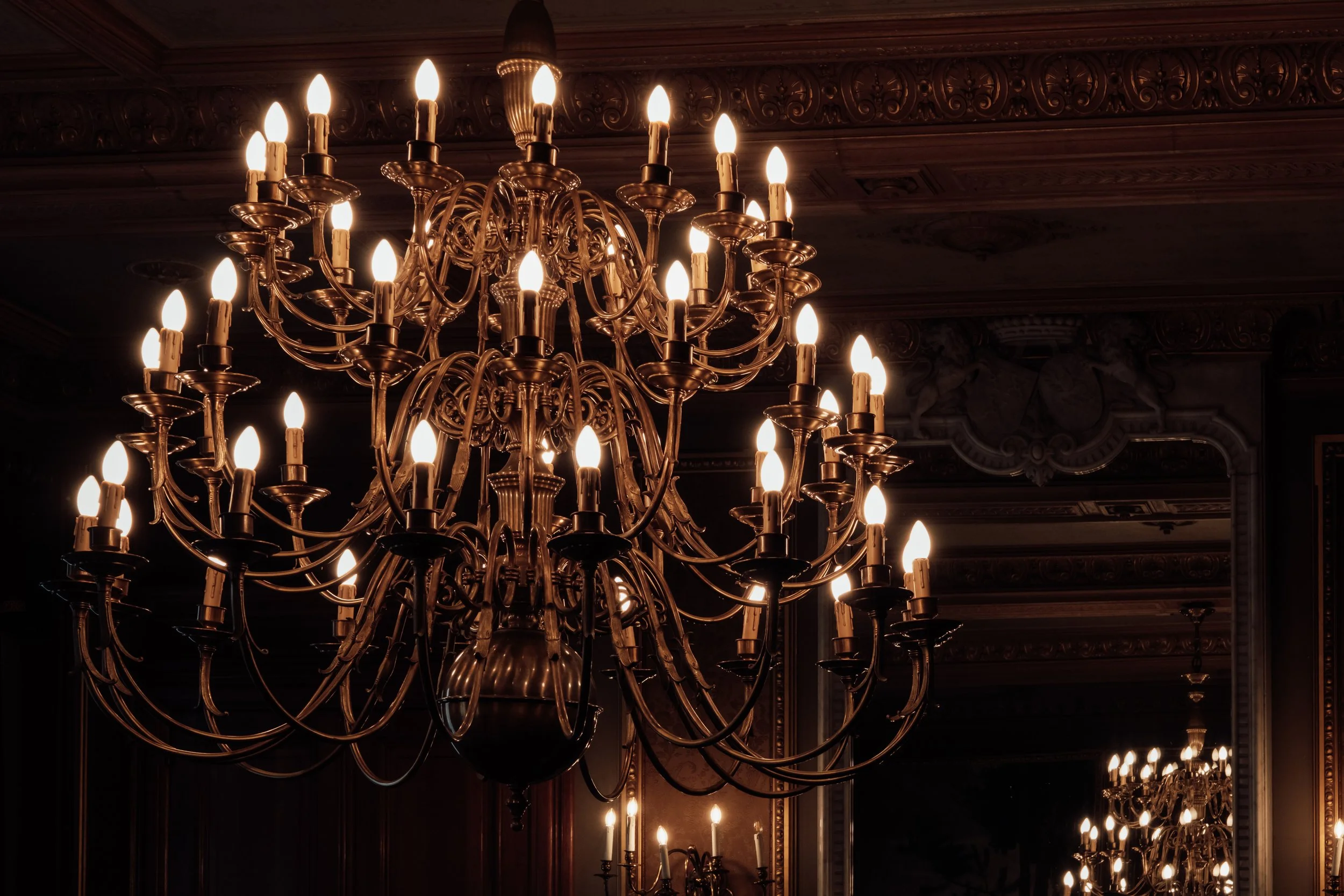 An ornate chandelier with multiple lit candles hanging from a decorative ceiling in a richly decorated room.