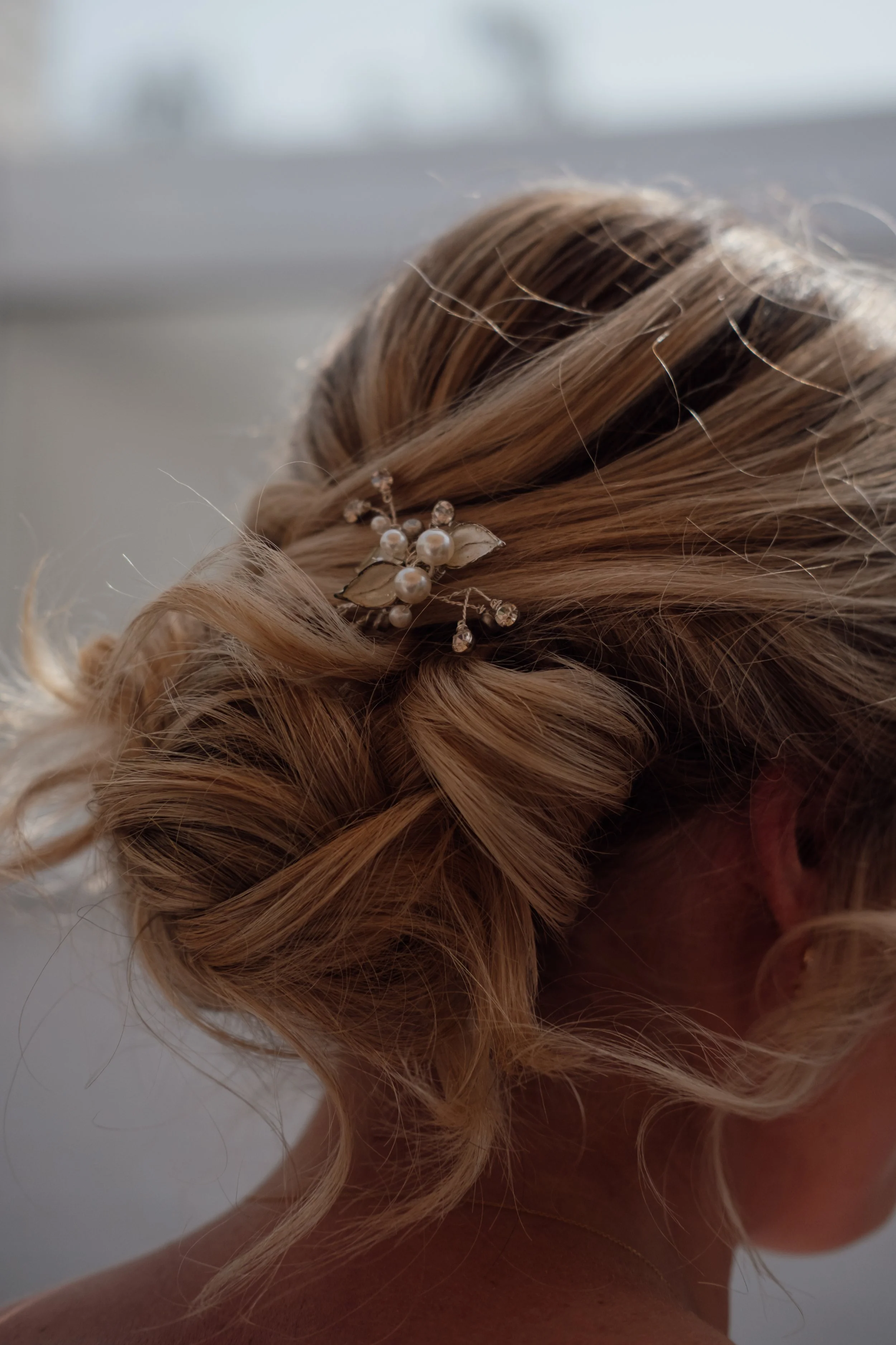Close-up of a woman's blonde, curly hair styled with a decorative hairpin featuring pearls and rhinestones.