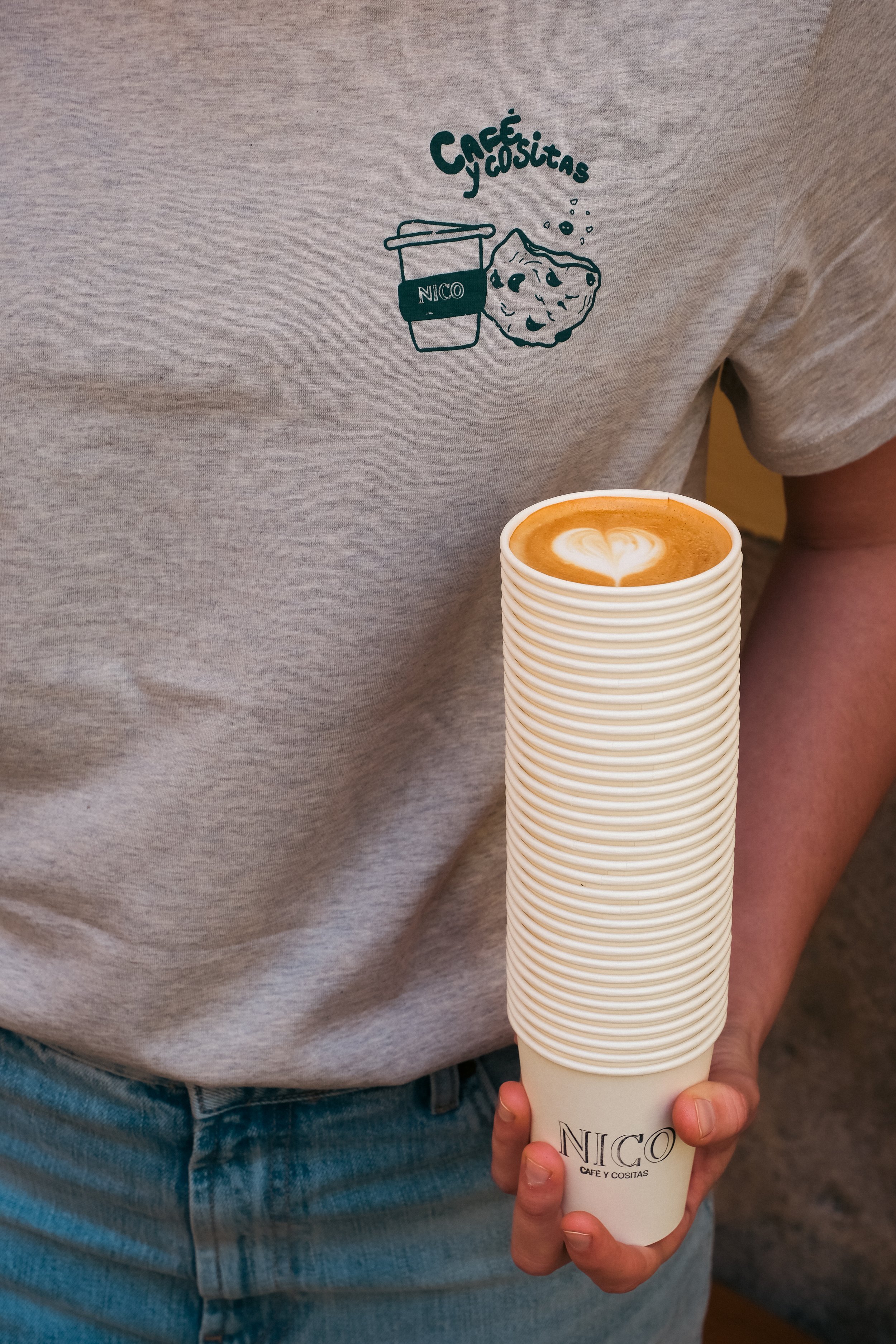 Girl holding coffee cups and wearing a branded grey shirt