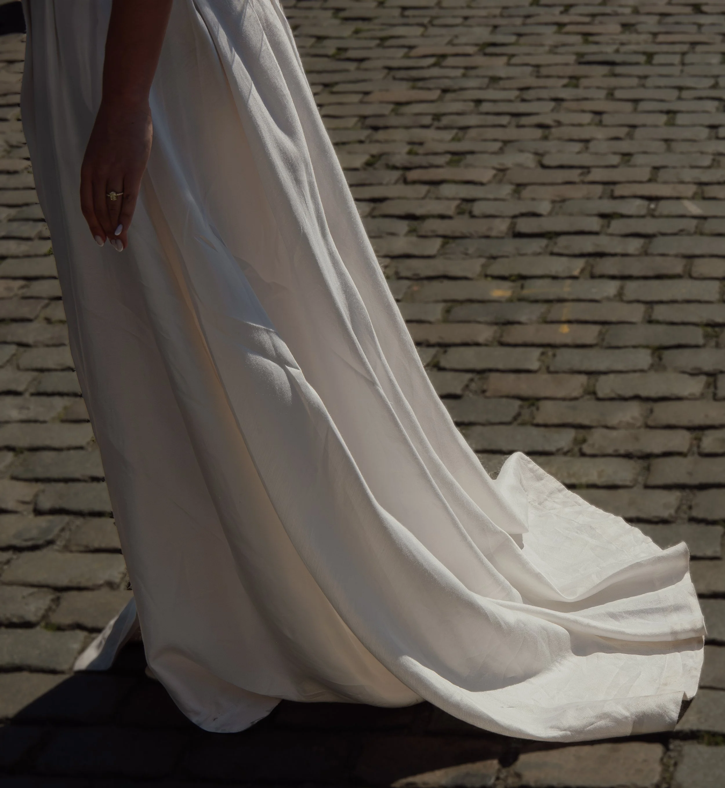 Close-up of a woman in a white dress with hand resting on her side, on a cobblestone path.
