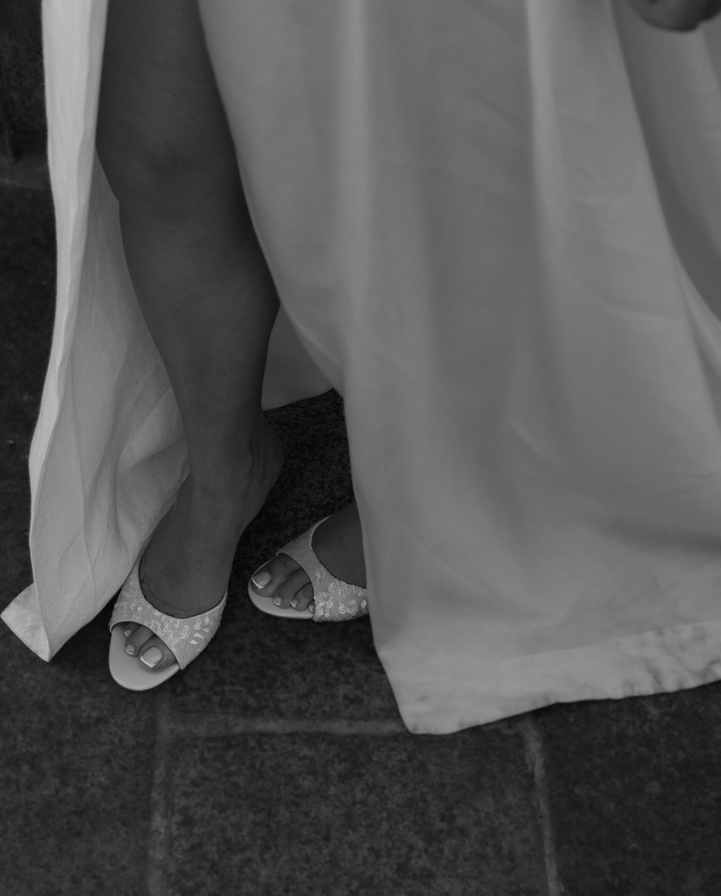 A person wearing dress shoes and lace socks standing on dark flooring next to a white curtain.