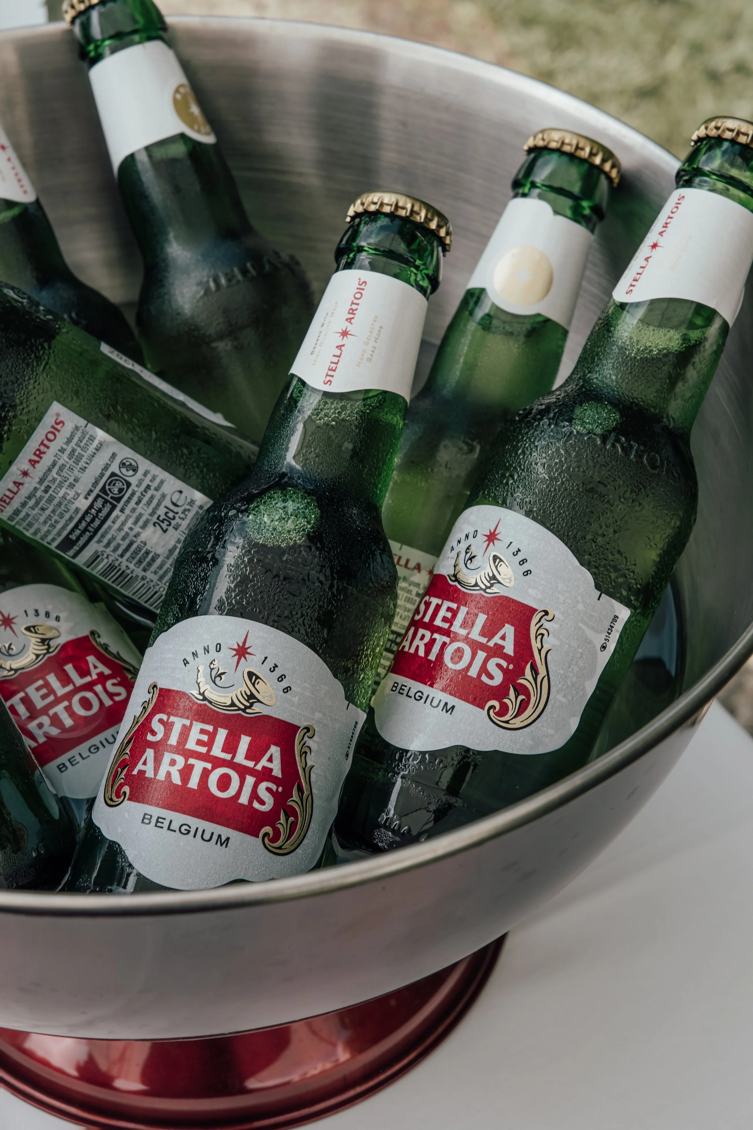 Several green glass beer bottles labeled Stella Artois, placed in a metallic ice bucket with condensation on the bottles.