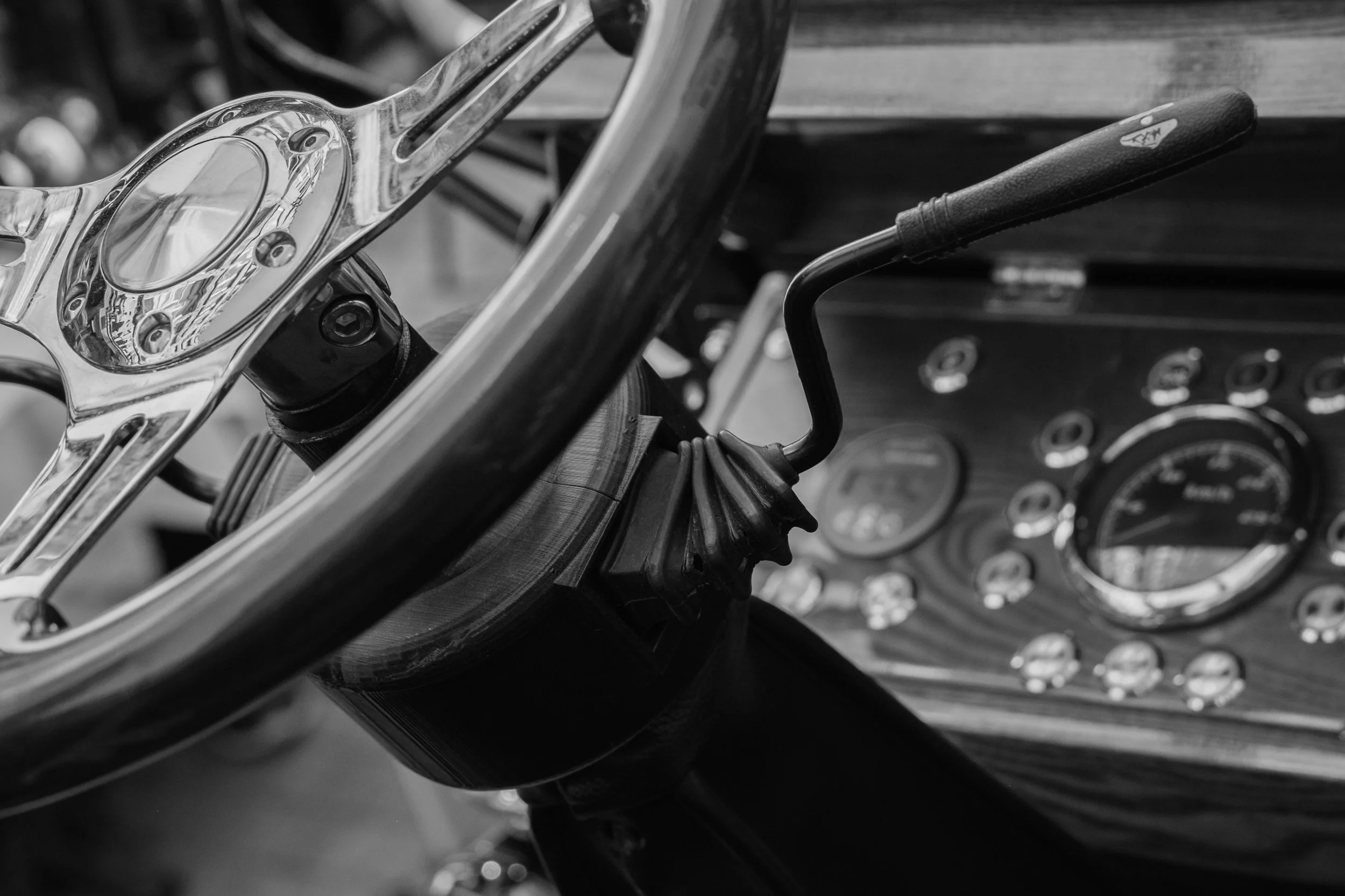 Close-up black and white photo of a vintage motorcycle suspension system and a section of the wheel, with a focus on the detailed metal parts and gauges in the background.