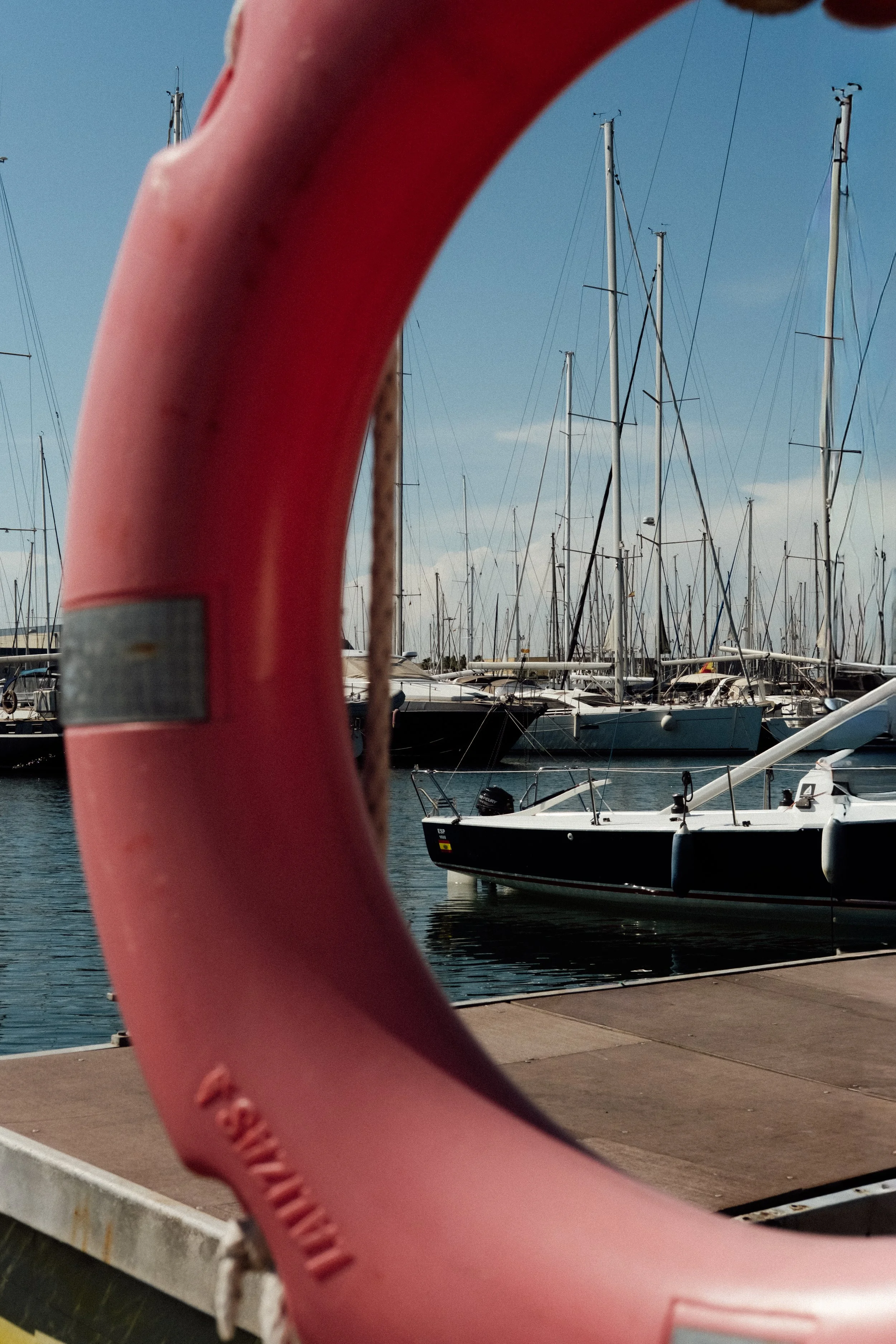 Wave runner with a pink exterior in the foreground, sailing boats docked in the harbor in the background under a clear blue sky.