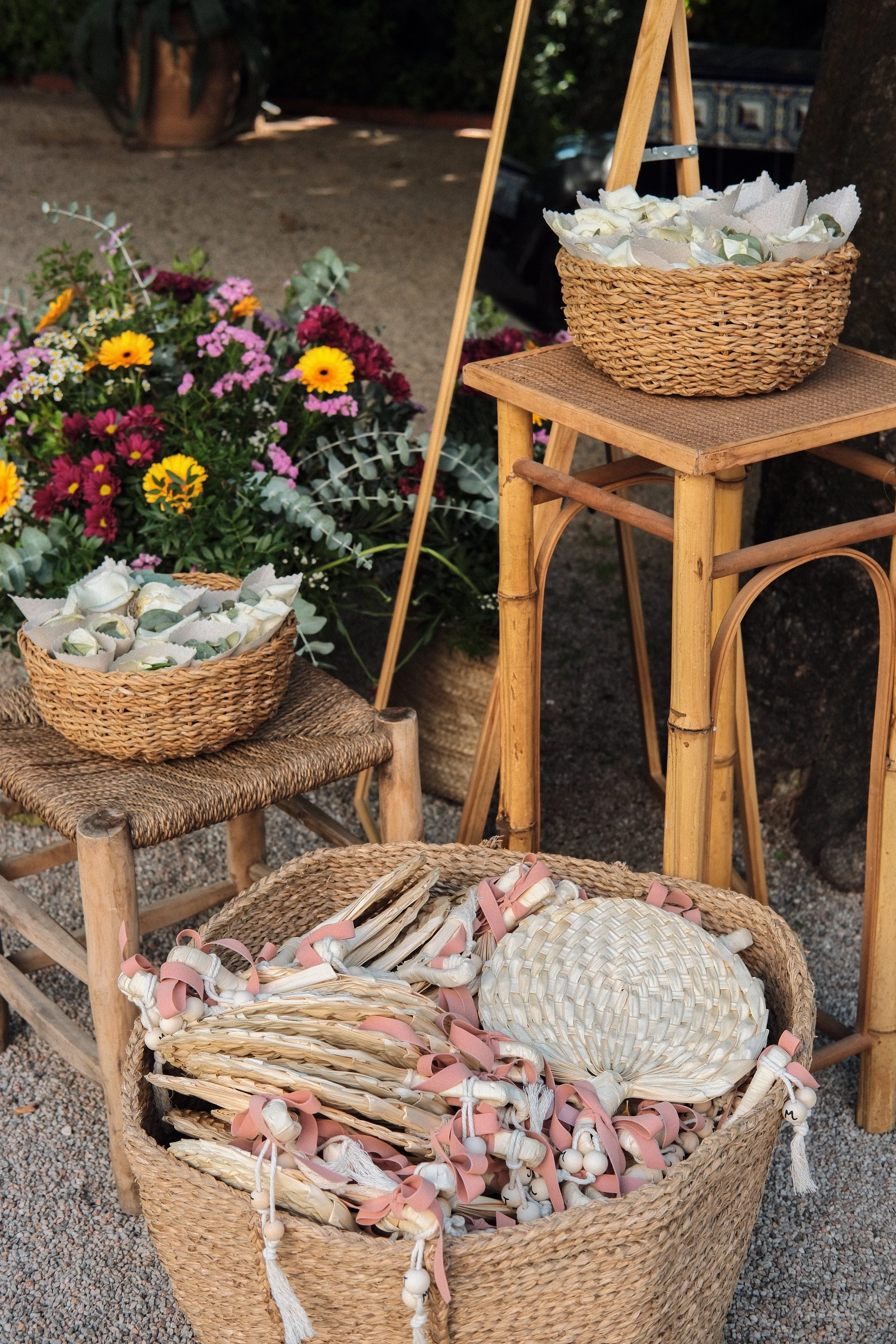 A large woven basket filled with decorative ribbons and pom-poms, sitting on a wicker stool outdoors.